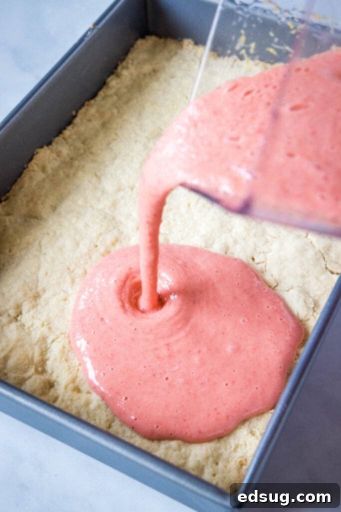 Bright & Tangy Strawberry Lemonade Treats 4 Strawberry lemon filling being carefully poured over a golden-baked shortbread crust in a baking pan.