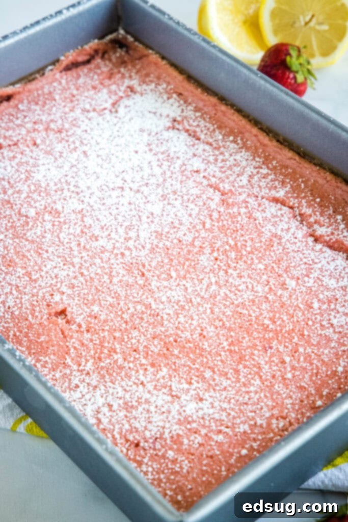 Bright & Tangy Strawberry Lemonade Treats 5 Freshly baked strawberry lemon bars in a baking pan, generously dusted with powdered sugar and ready to be sliced.