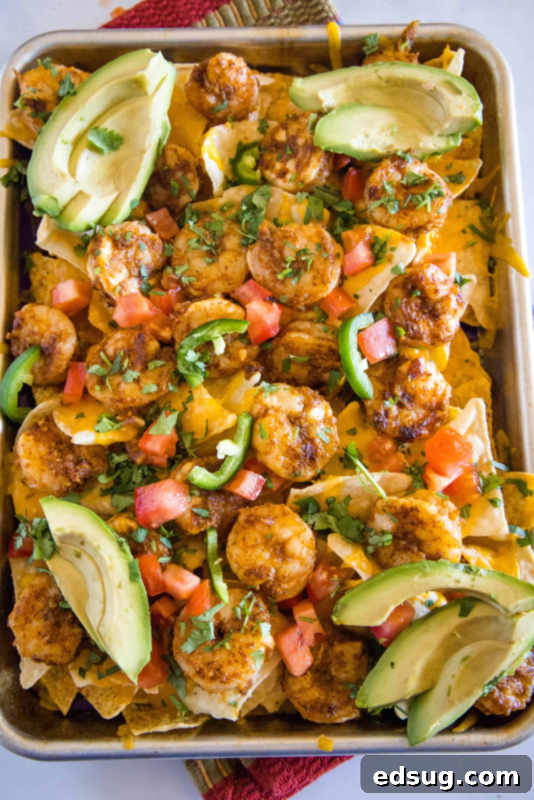 Upgrade classic nachos with zesty seasoned shrimp! These shrimp nachos are an easy Tex-Mex appetizer packed with flavor, ready in 15 minutes. Overhead view of shrimp nachos on a sheet pan garnished with avocado slices.