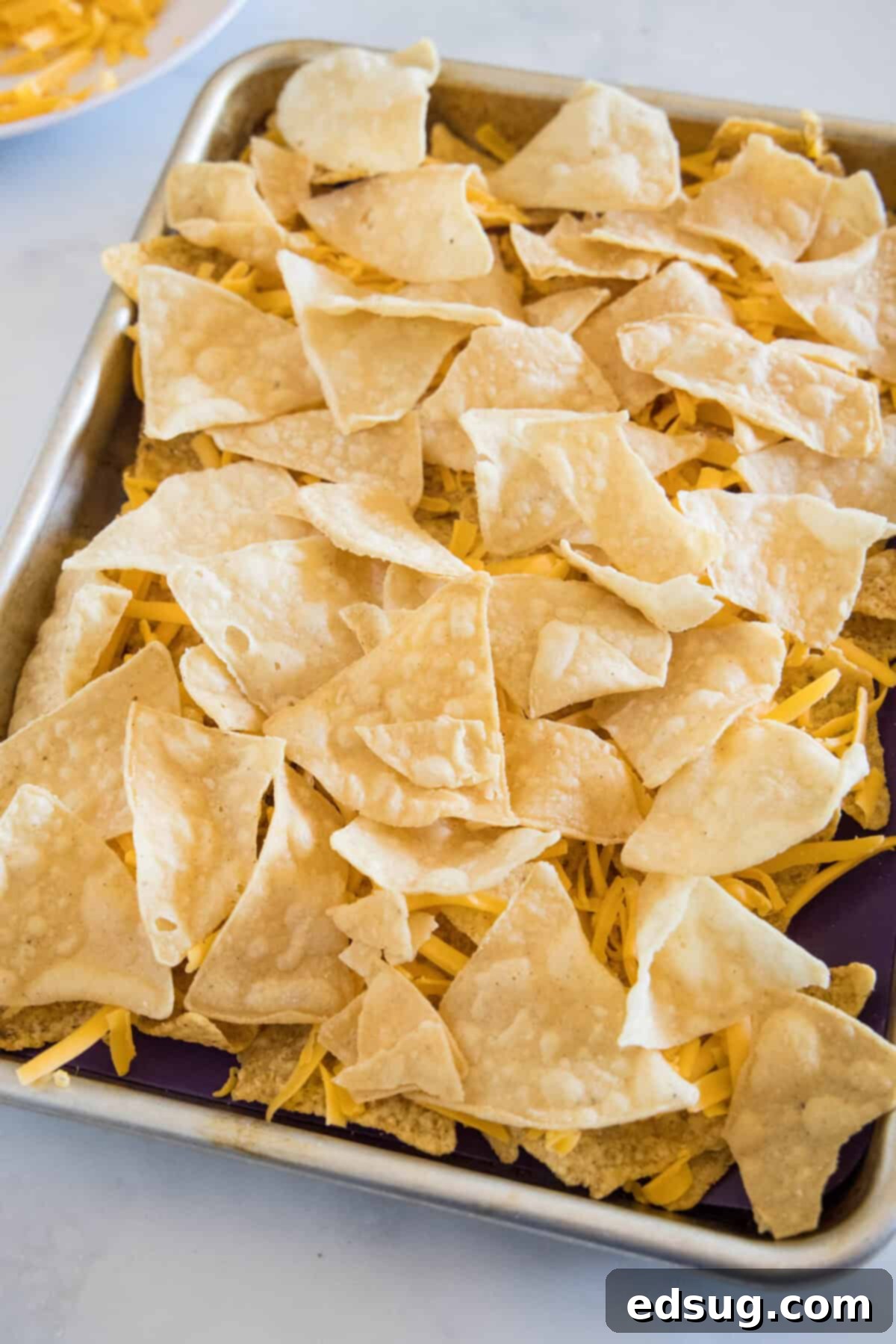 Upgrade classic nachos with zesty seasoned shrimp! These shrimp nachos are an easy Tex-Mex appetizer packed with flavor, ready in 15 minutes. Tortilla chips layered with shredded cheese on a sheet pan.