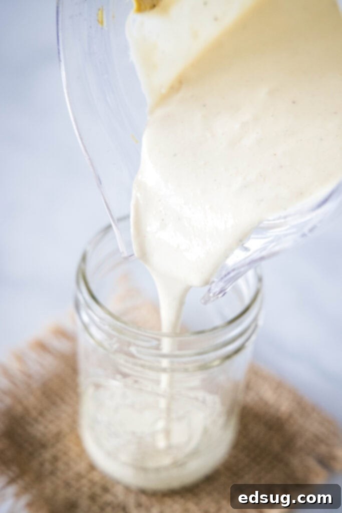 Signature Grilled Chicken Caesar 5 Pouring freshly blended, creamy Caesar dressing from a blender into a glass jar for storage, showcasing its smooth texture.