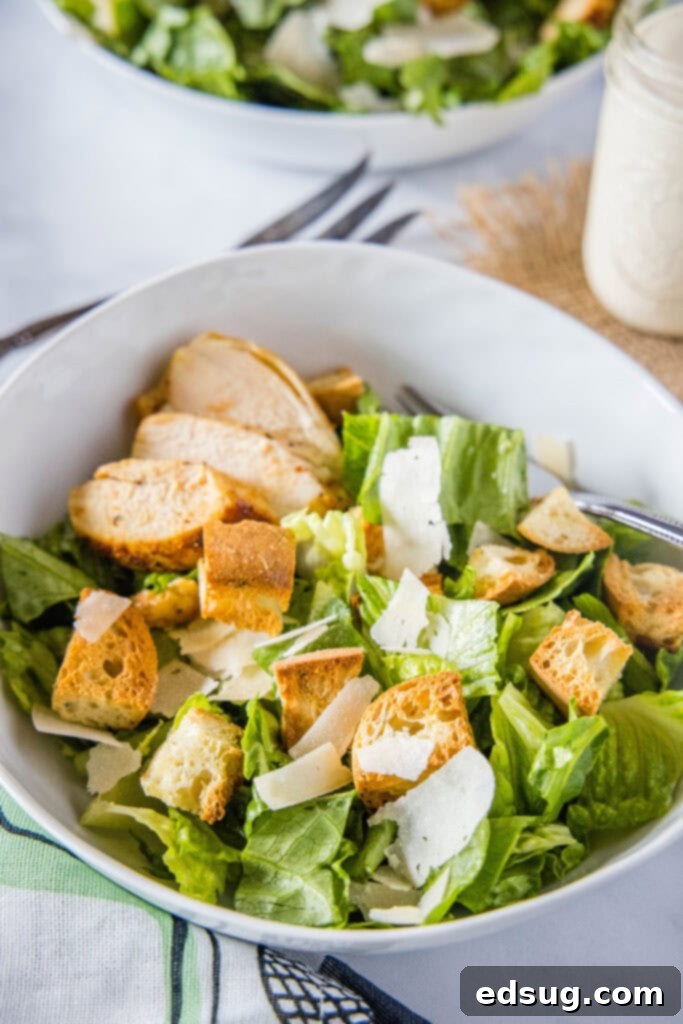 Signature Grilled Chicken Caesar 7 A small bowl of chicken Caesar salad, with a mason jar filled with Caesar dressing blurred in the background, creating a cozy kitchen scene.