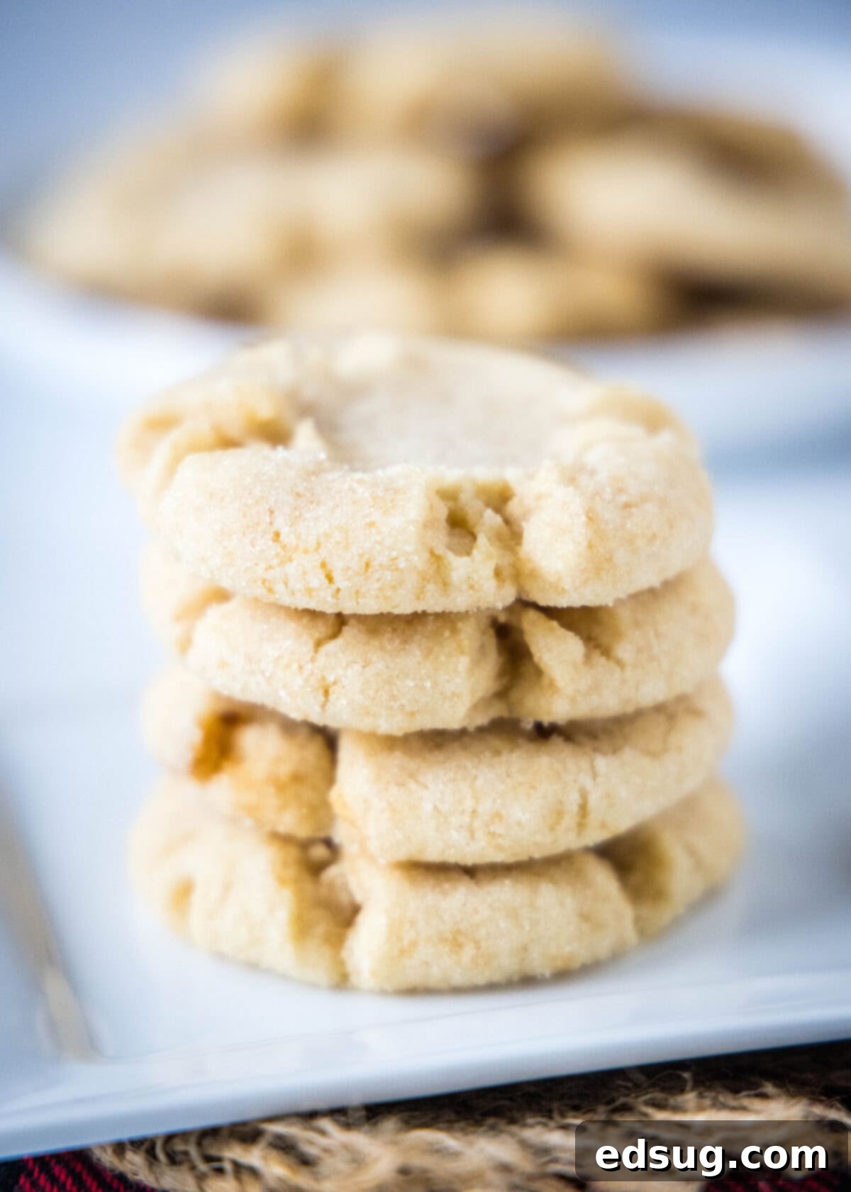 A warm stack of golden Angel Crisp sugar cookies artfully arranged on a white plate, showcasing their delicate cracks and glistening sugar coating, inviting a taste.