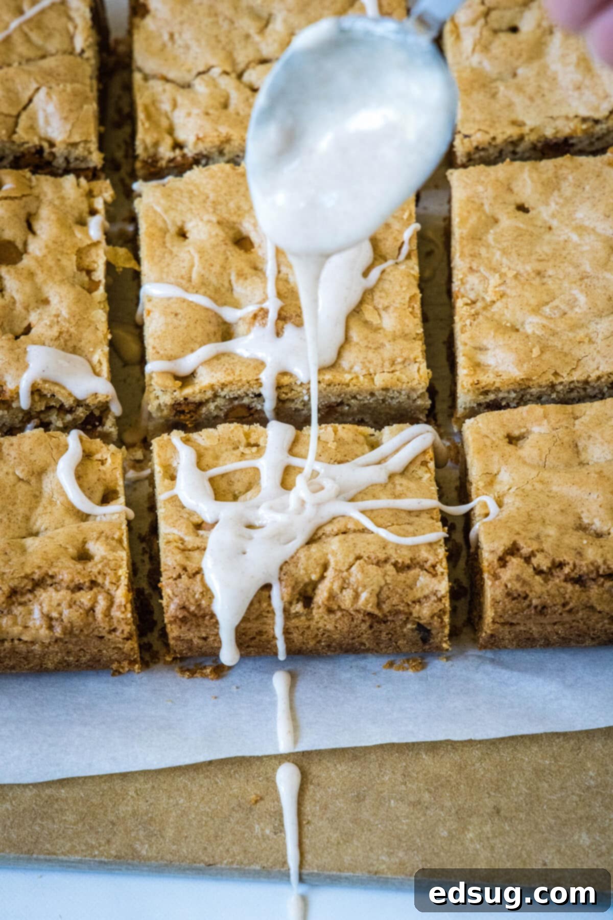 Cozy Cinnamon Blondies 6 A delicious cinnamon glaze being artfully drizzled over a tray of warm, golden cinnamon blondies, creating an inviting pattern.