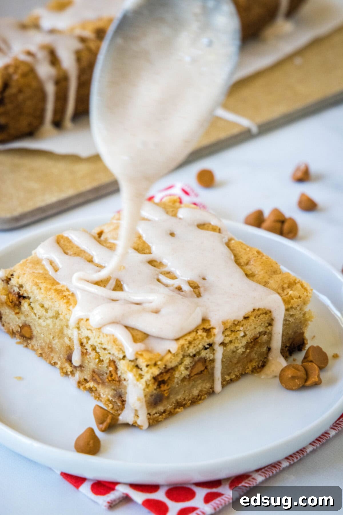 Cozy Cinnamon Blondies 7 A single cinnamon blondie on a white plate being drizzled with a smooth cinnamon glaze, ready to be enjoyed.