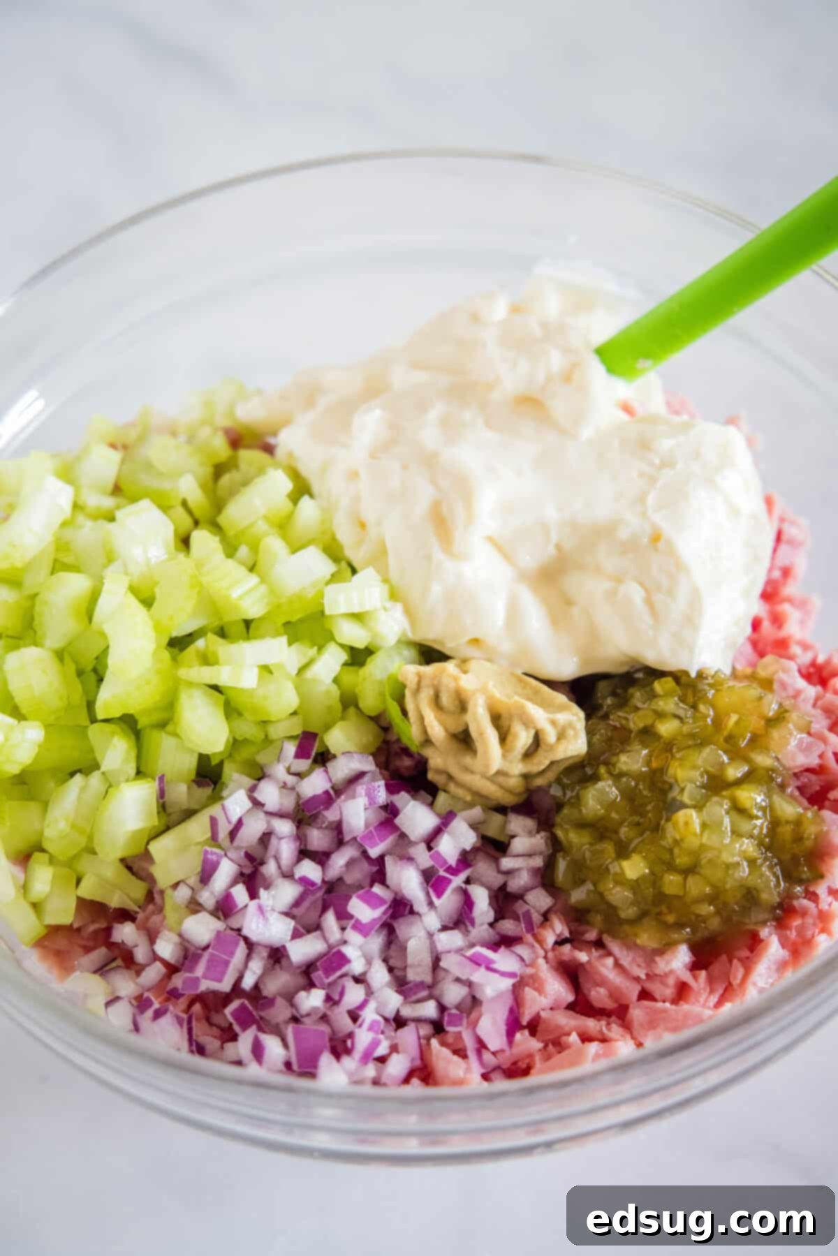 This ham salad recipe is the best way to use up leftover ham! It's similar to a chicken salad, with mayo, red onions, and juicy shredded ham. Ham salad ingredients combined in a bowl.