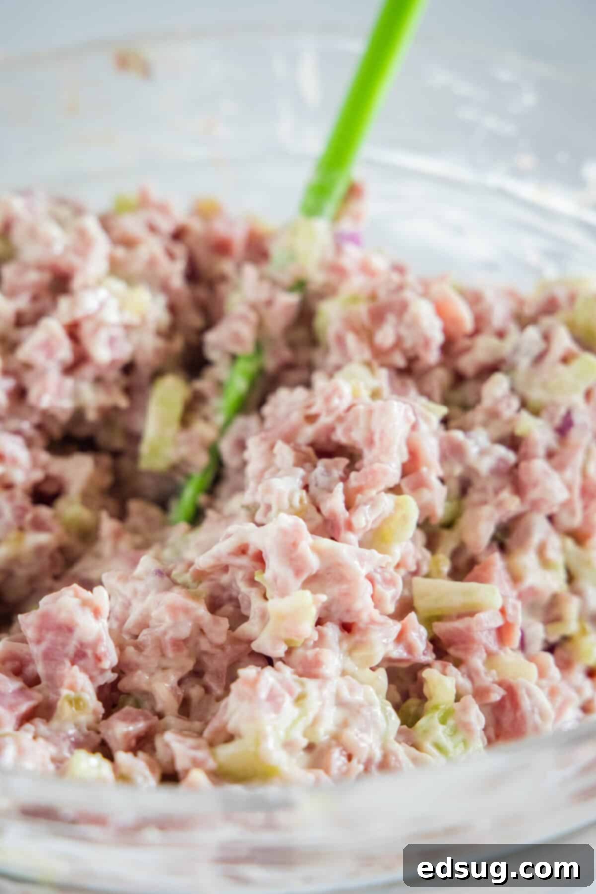 This ham salad recipe is the best way to use up leftover ham! It's similar to a chicken salad, with mayo, red onions, and juicy shredded ham. Ham salad ingredients combined with the dressing in a bowl.