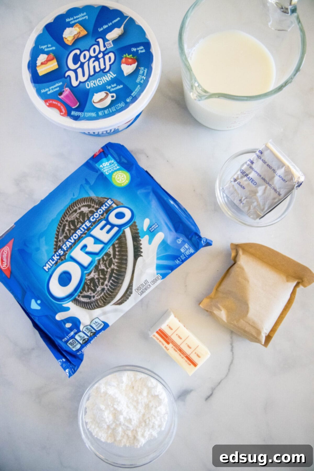 Overhead view of the essential ingredients laid out for making no-bake Oreo lasagna: a package of Oreo cookies, a tub of Cool Whip, a box of instant chocolate pudding mix, a glass measuring cup with milk, a bowl of softened cream cheese, a bowl of powdered sugar, and a portion of melted butter.