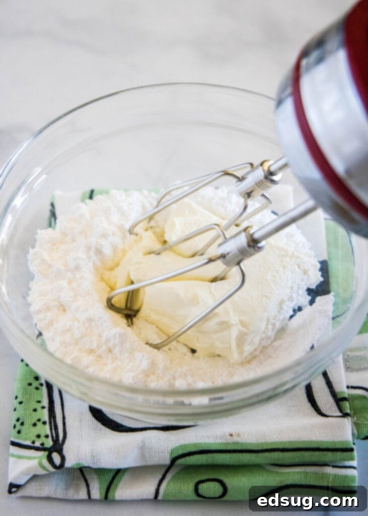 A beater mixing softened cream cheese and powdered sugar in a bowl, creating a smooth and fluffy texture for the middle layer of the Oreo lasagna.