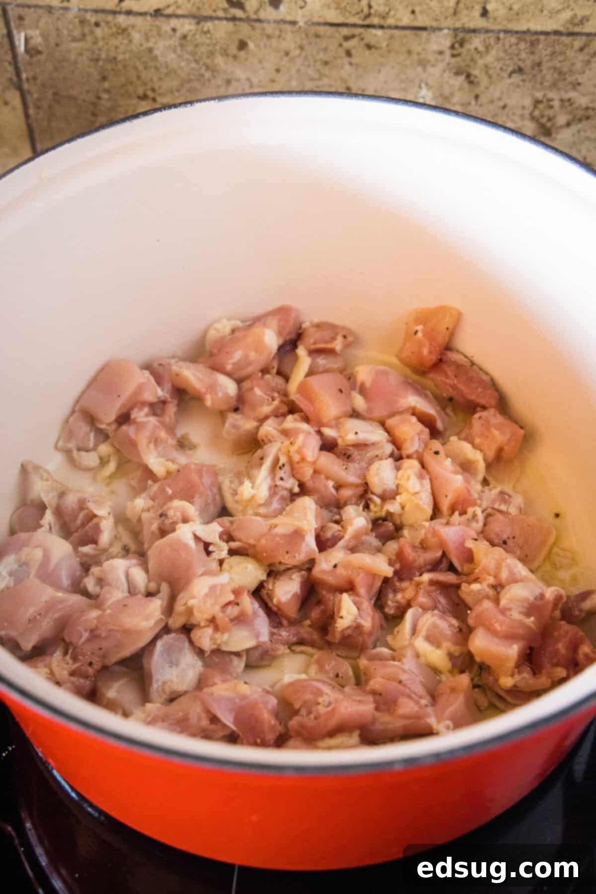 Chicken pieces searing in a large pot with olive oil.
