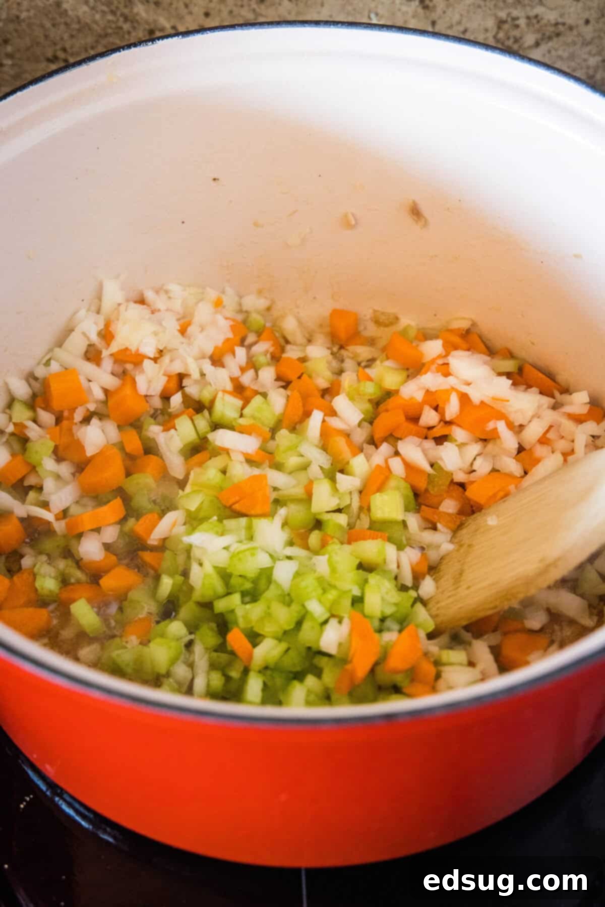 Sautéed carrots, celery, and onion cooking in a large pot with melted butter.