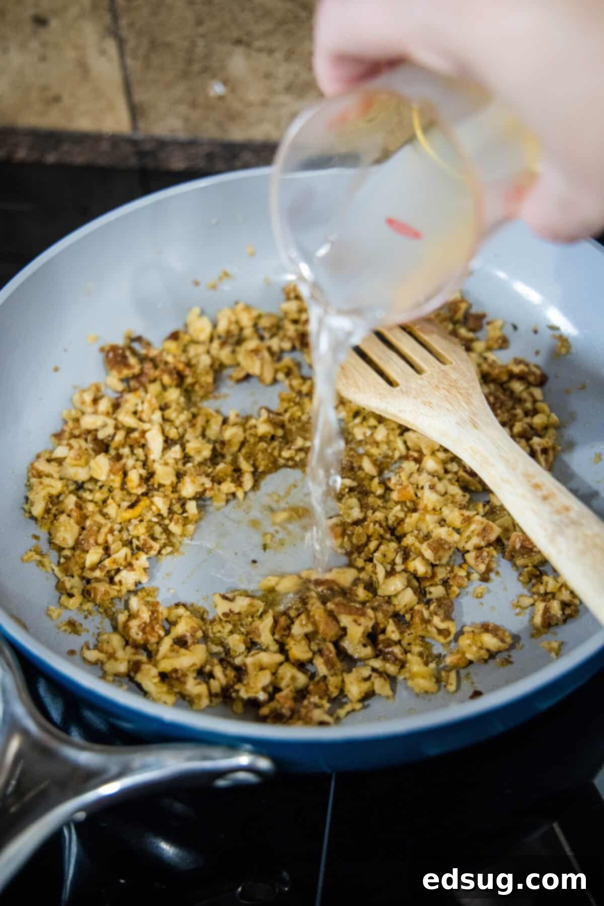 This toasted walnut pasta is an easy, flavorful, and filling 15-minute pasta recipe with crunchy walnuts, breadcrumbs, garlic, and chili. Starchy pasta water being added to the toasted walnut mixture in a skillet, creating a light sauce.