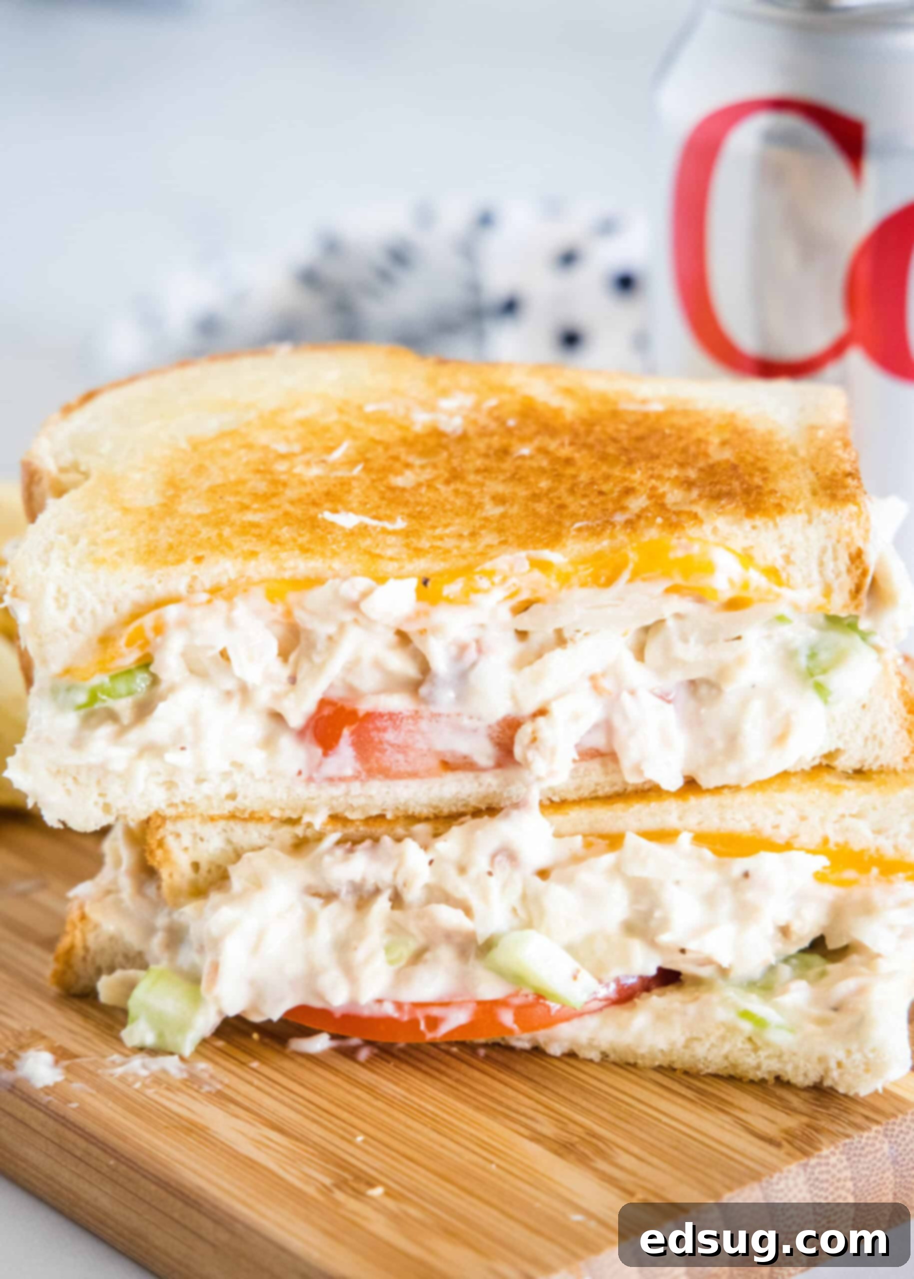 Two halves of a perfectly golden, crispy tuna melt stacked on a rustic wooden platter, revealing gooey melted cheese and fresh tomato slices.