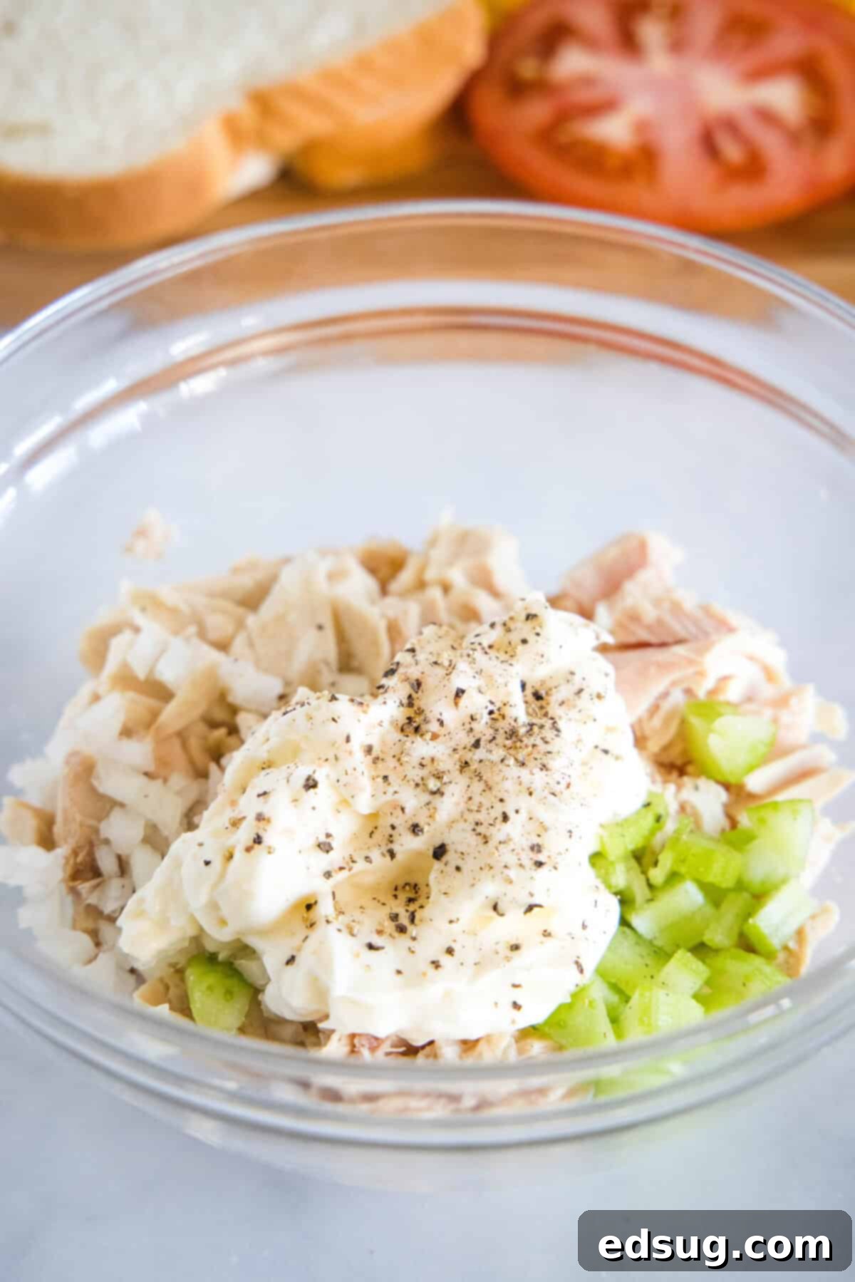 Drained tuna, mayonnaise, chopped celery, and diced onion ready to be mixed in a clear glass bowl, showcasing the fresh ingredients.