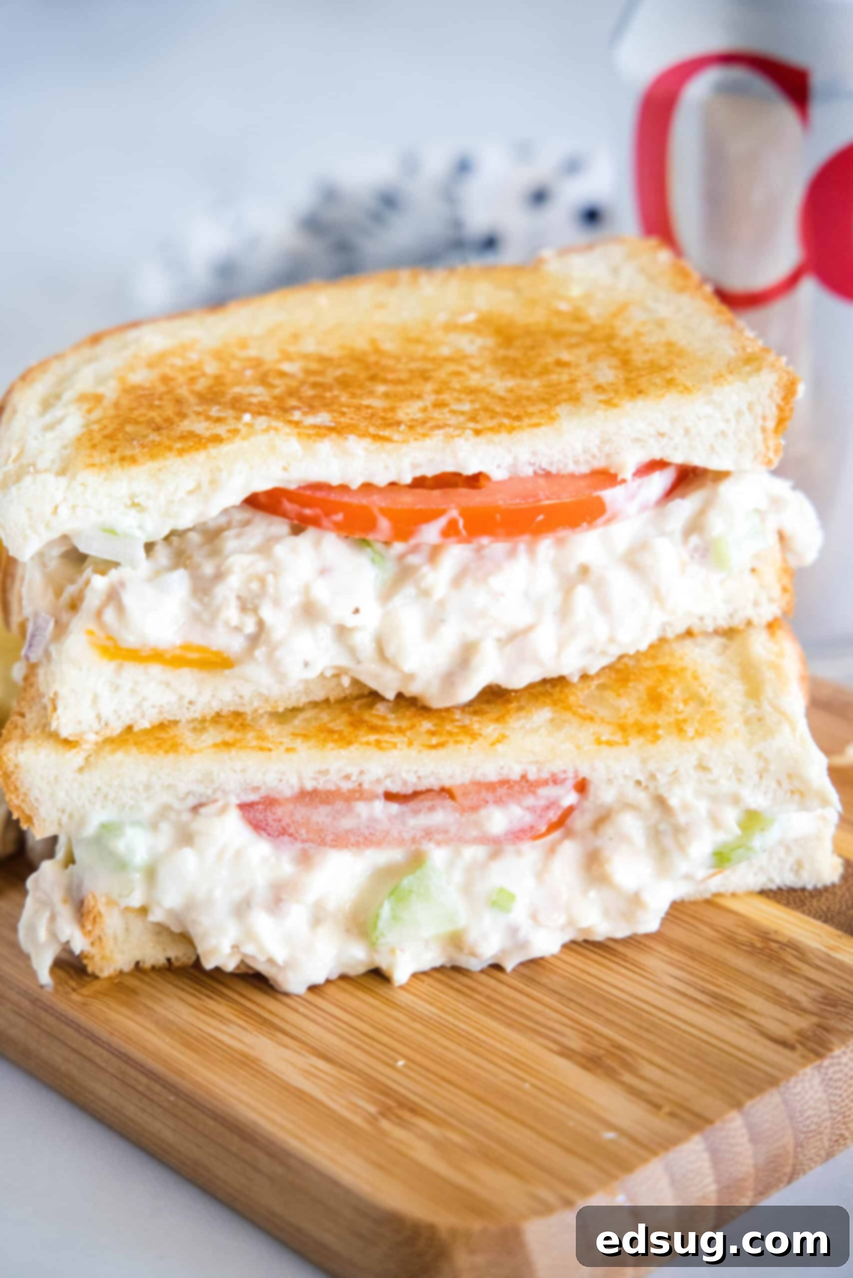 Two halves of a perfectly golden, crispy tuna melt stacked on a rustic wooden platter, showcasing the rich tuna salad, melted cheese, and fresh tomato slices.