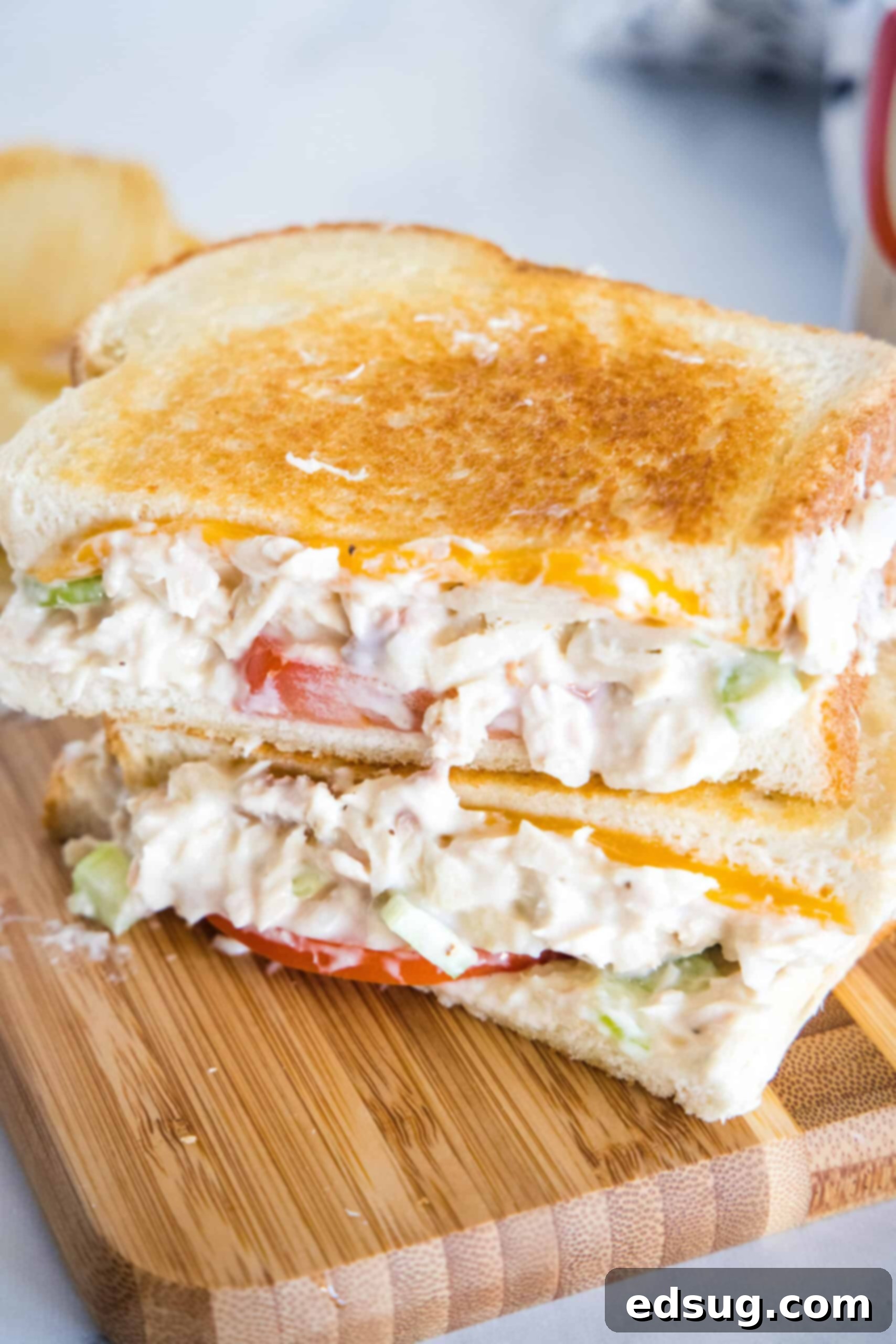 Two halves of a tuna melt stacked on top of one another on a wooden platter, showcasing the melted cheese and fresh ingredients, ready to be enjoyed.