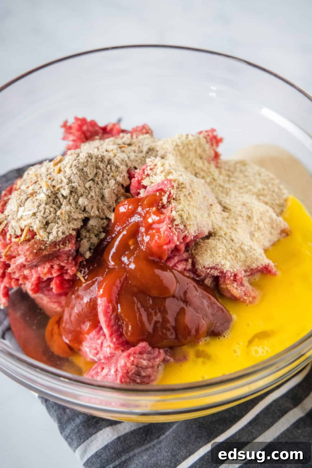 Onion soup meatloaf ingredients combined in a glass mixing bowl. Onion soup meatloaf ingredients combined in a glass mixing bowl.
