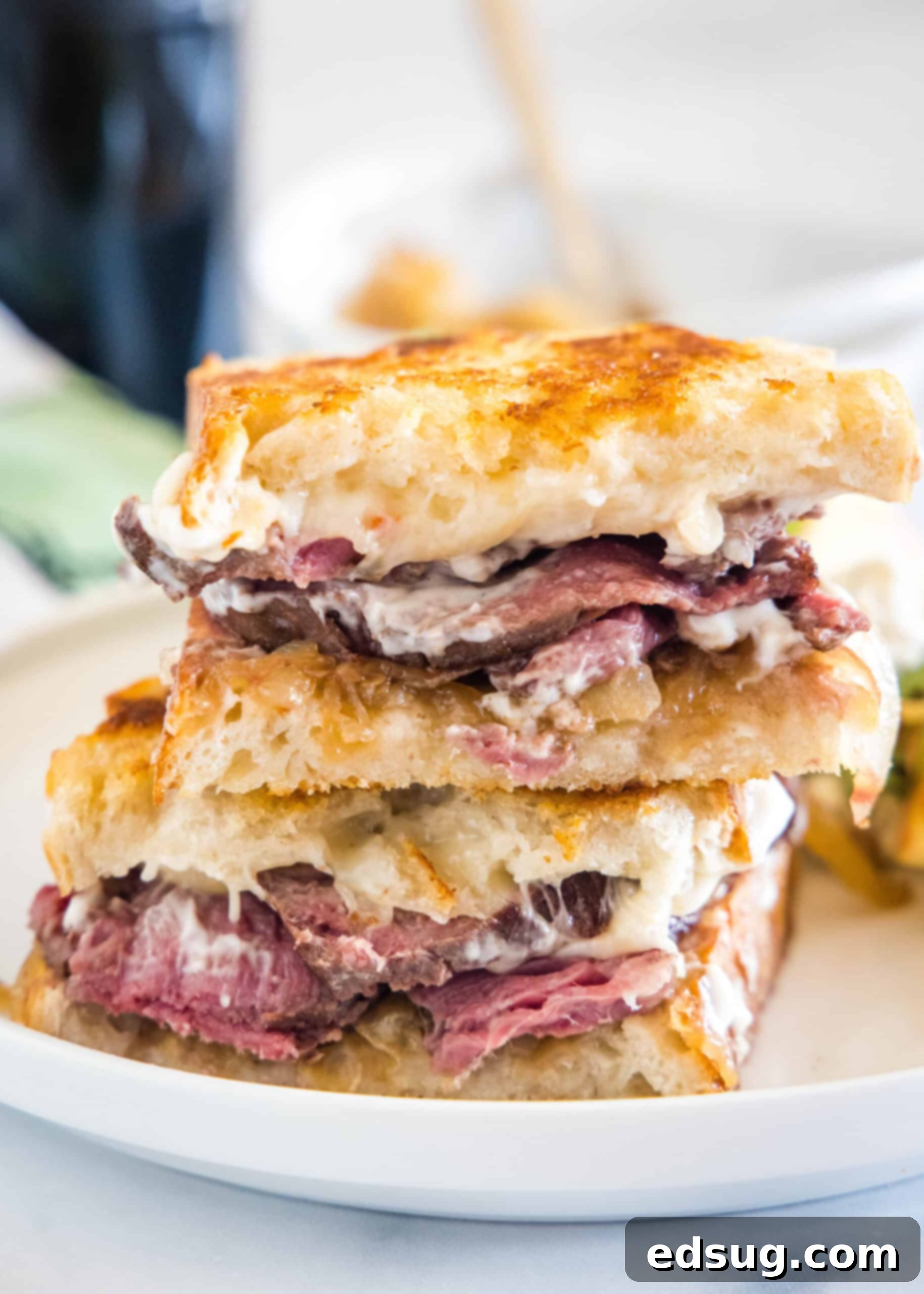 Two halves of a steak sandwich stacked on a white plate, showcasing the juicy beef, melted cheese, and golden-brown bread.