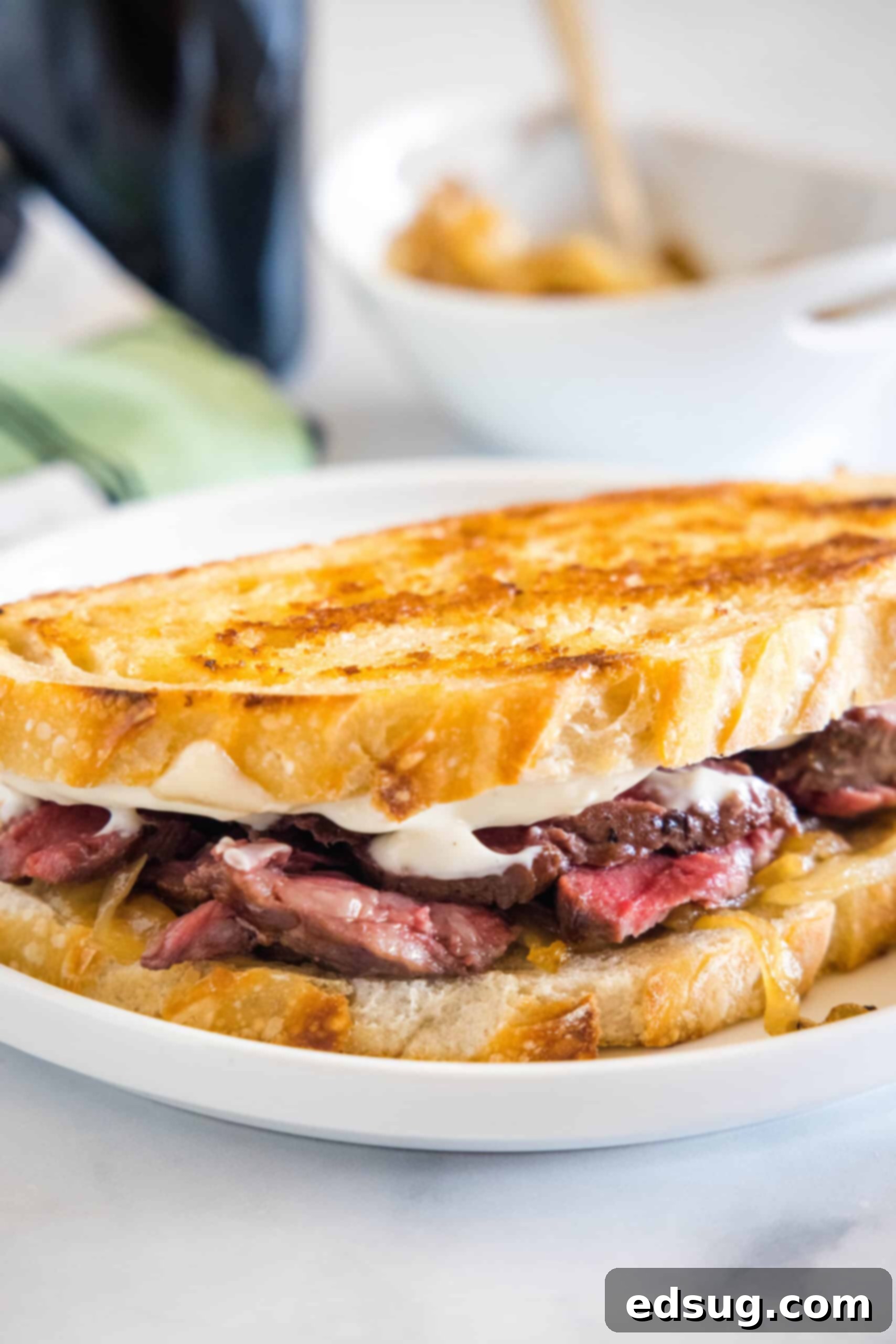 A perfectly toasted steak sandwich, cut in half and ready to eat, served on a pristine white plate.