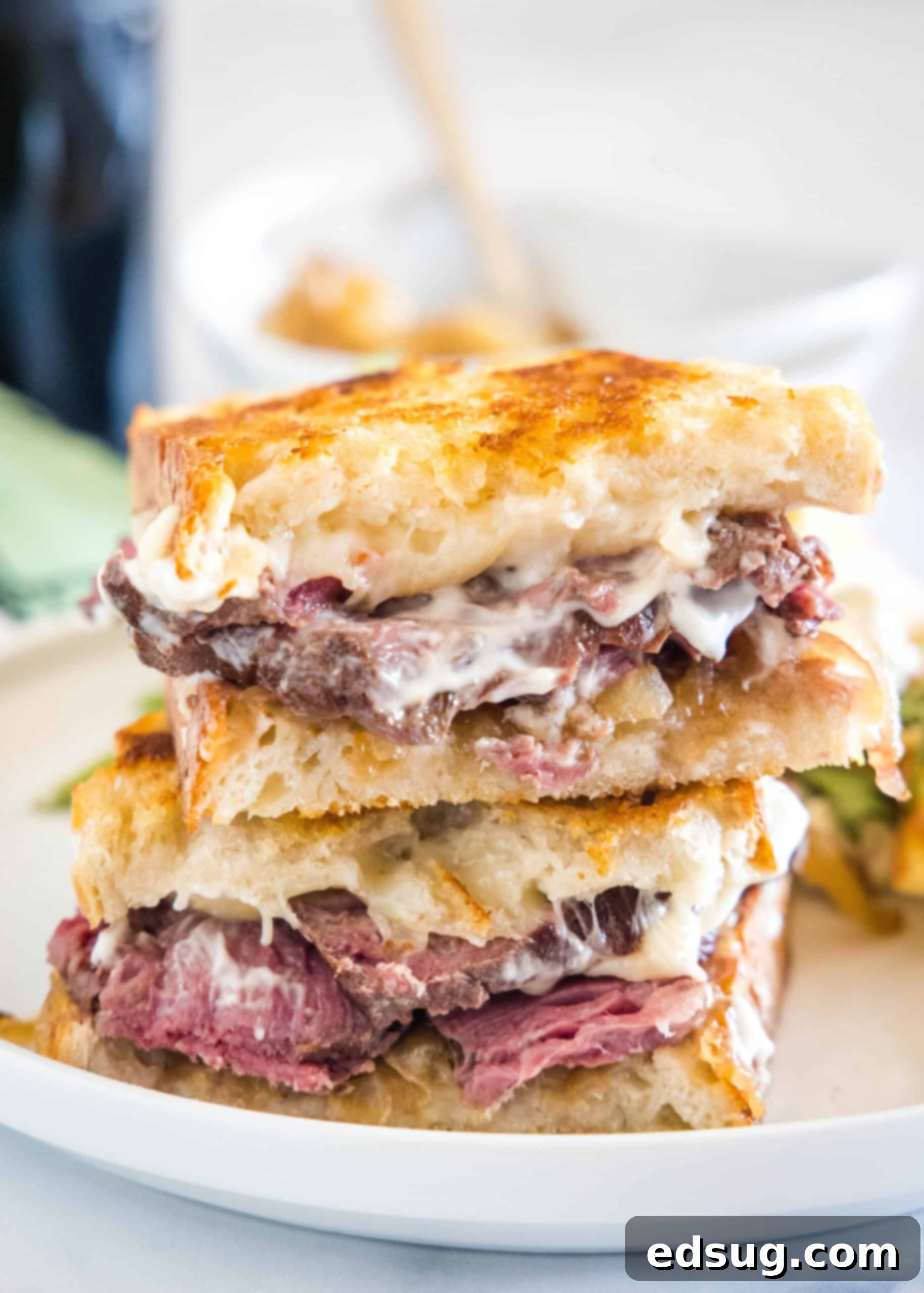 A stacked, golden-brown steak sandwich, cut in half, presented on a minimalist white plate.