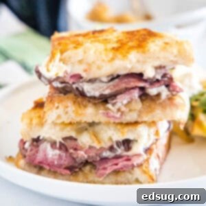 Two halves of a steak sandwich stacked on a white plate.