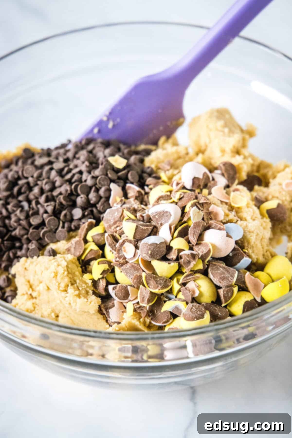 Ultimate Cadbury Mini Egg Cookies 3 adding chocolate chips and mini eggs to cookie dough in a mixing bowl