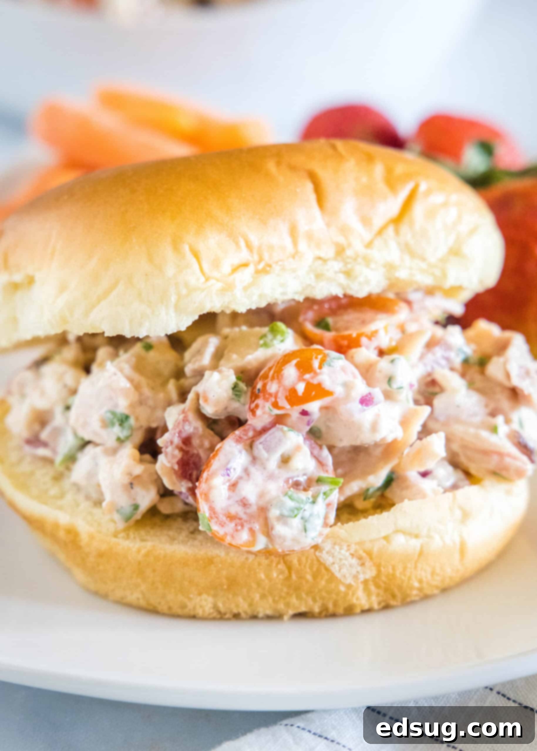This BLT chicken salad is loaded with juicy shredded chicken, bacon, cherry tomatoes, and crispy red onion tossed with creamy mayo dressing. A BLT chicken salad sandwich on a fluffy bun on a white plate.