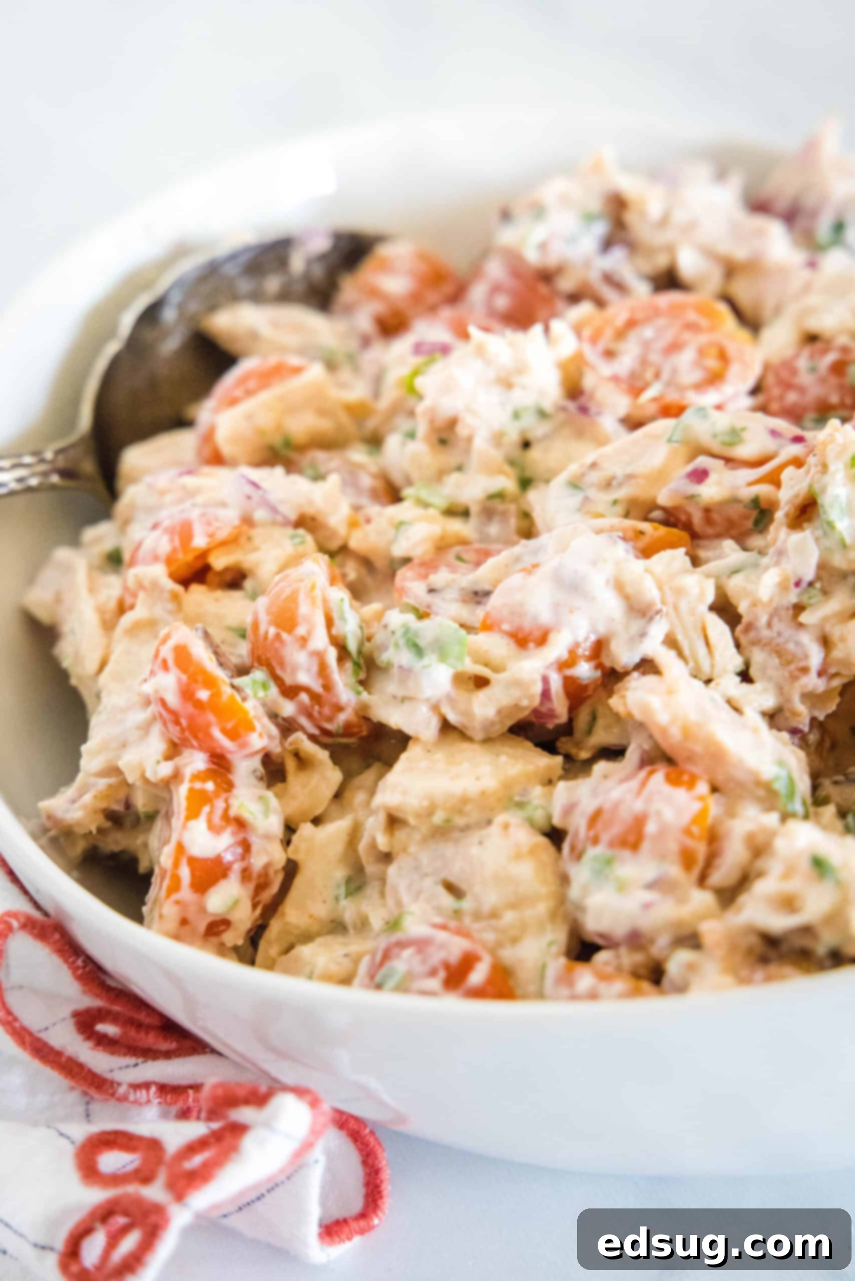 This BLT chicken salad is loaded with juicy shredded chicken, bacon, cherry tomatoes, and crispy red onion tossed with creamy mayo dressing. Close up of BLT chicken salad in a white bowl with a serving spoon.