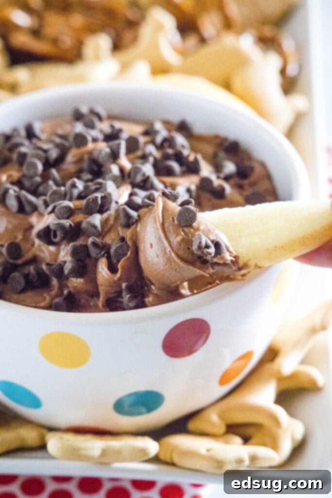A hand dipping a fresh apple slice into a bowl of brownie batter dip, highlighting a healthier, yet equally delicious, serving suggestion.
