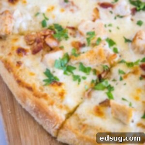 Close up of a chicken alfredo pizza cut into slices on a wooden butting board.