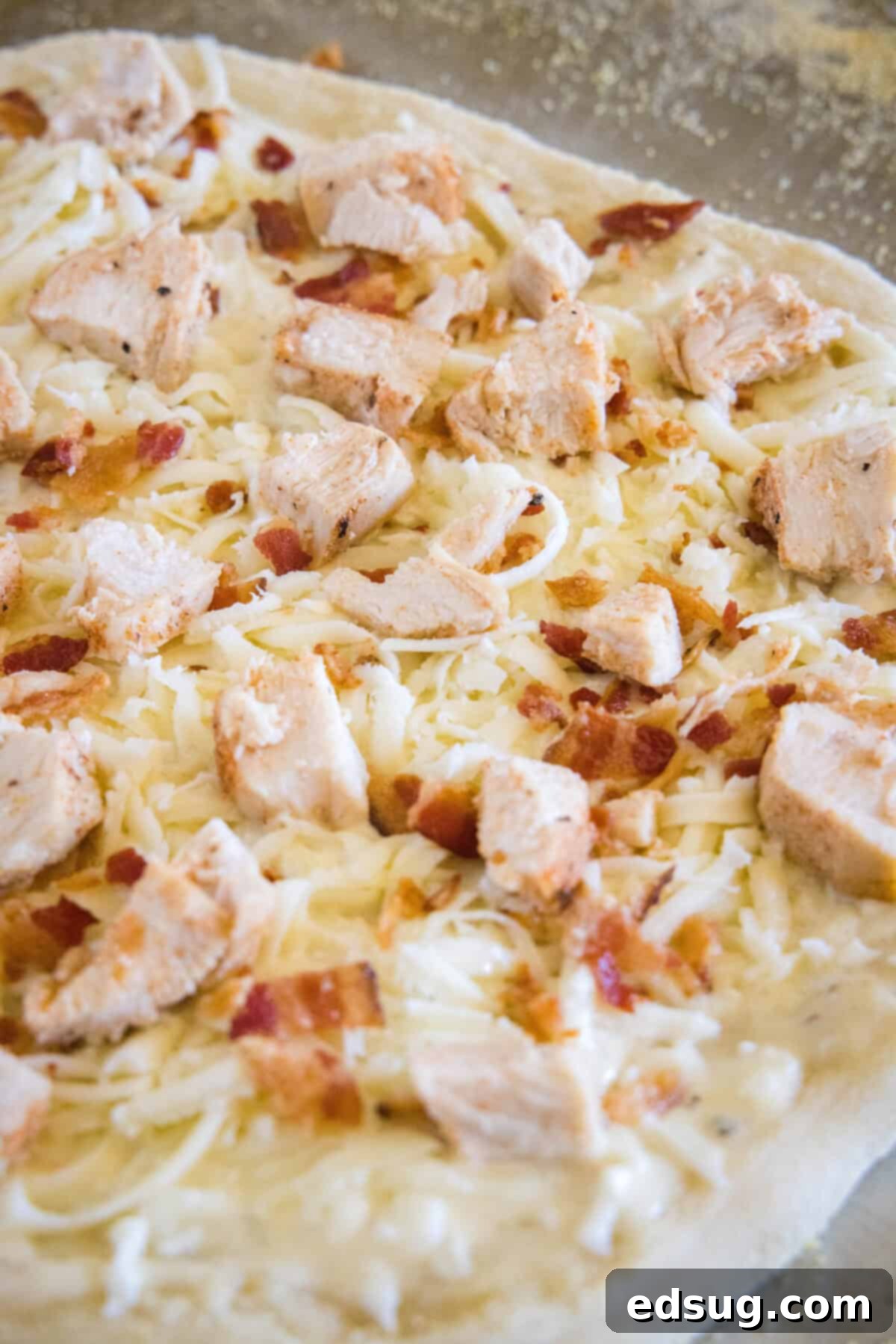 Chicken alfredo pizza fully assembled with chicken, bacon, and mozzarella cheese before baking.