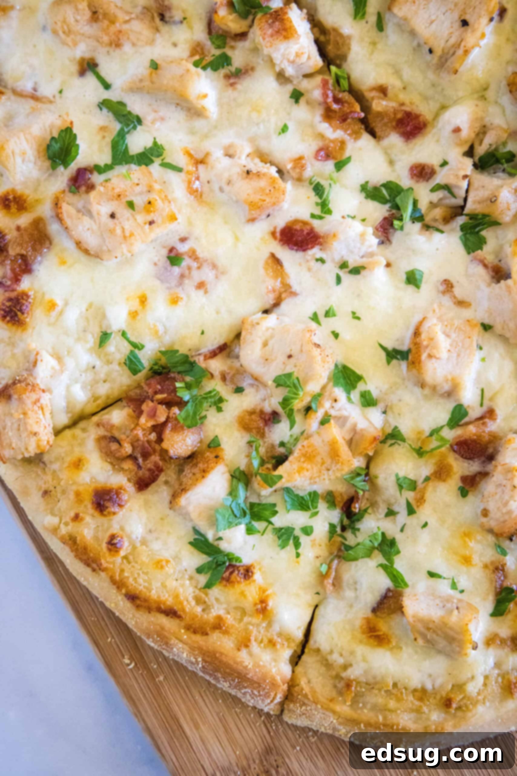 Full chicken alfredo pizza, cut into slices, on a wooden cutting board with a pizza cutter next to it.
