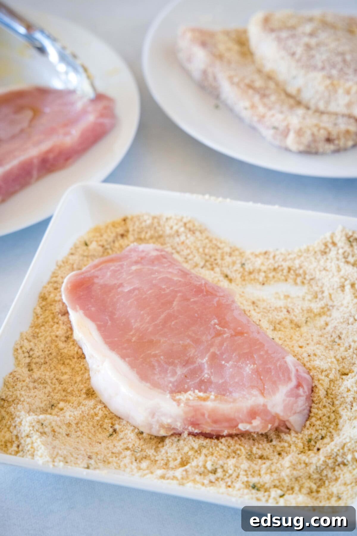 Hand pressing a boneless pork chop into a mixture of Parmesan cheese and breadcrumbs.