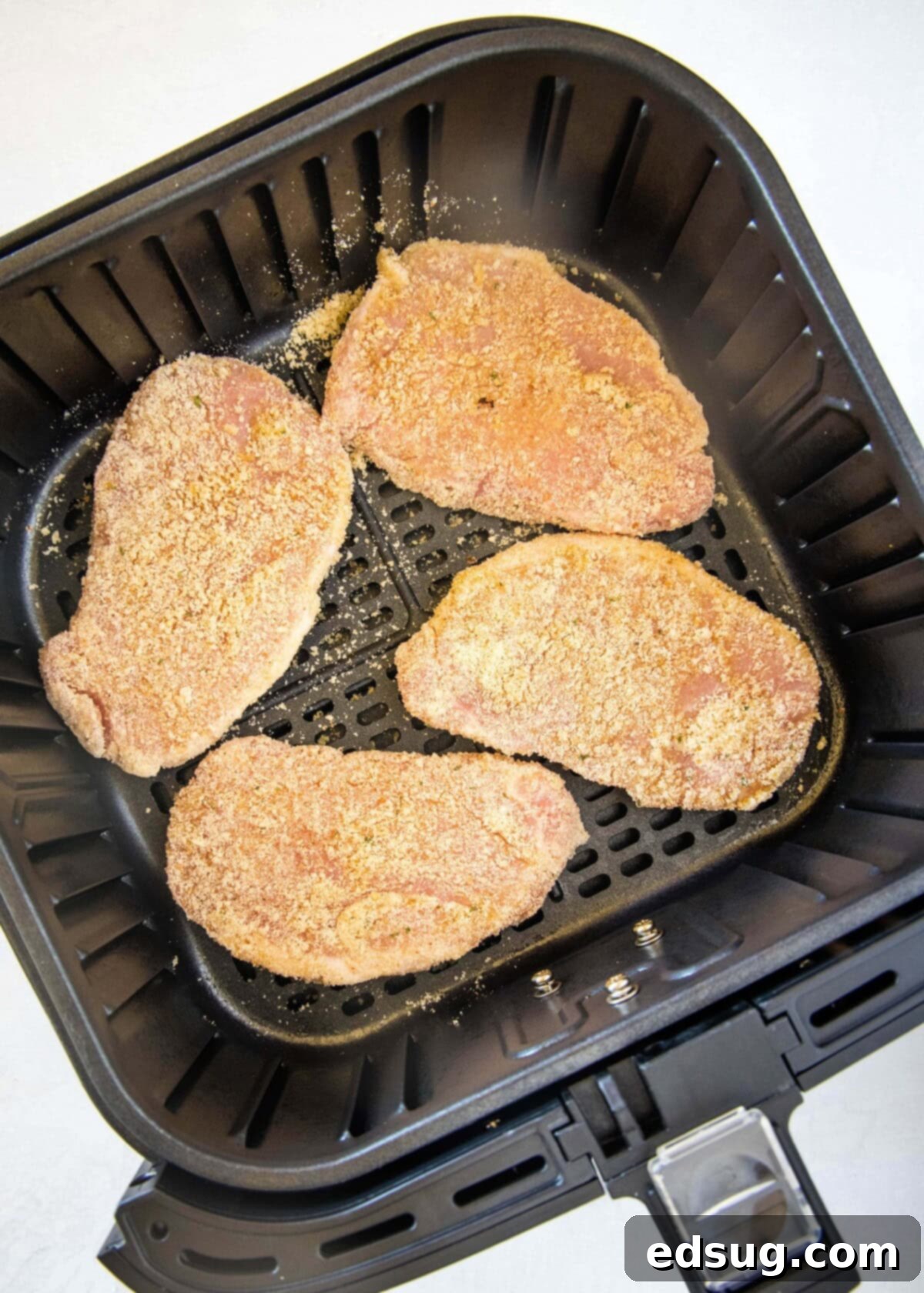 Coated boneless pork chops arranged in a single layer in an air fryer basket, ready to cook.