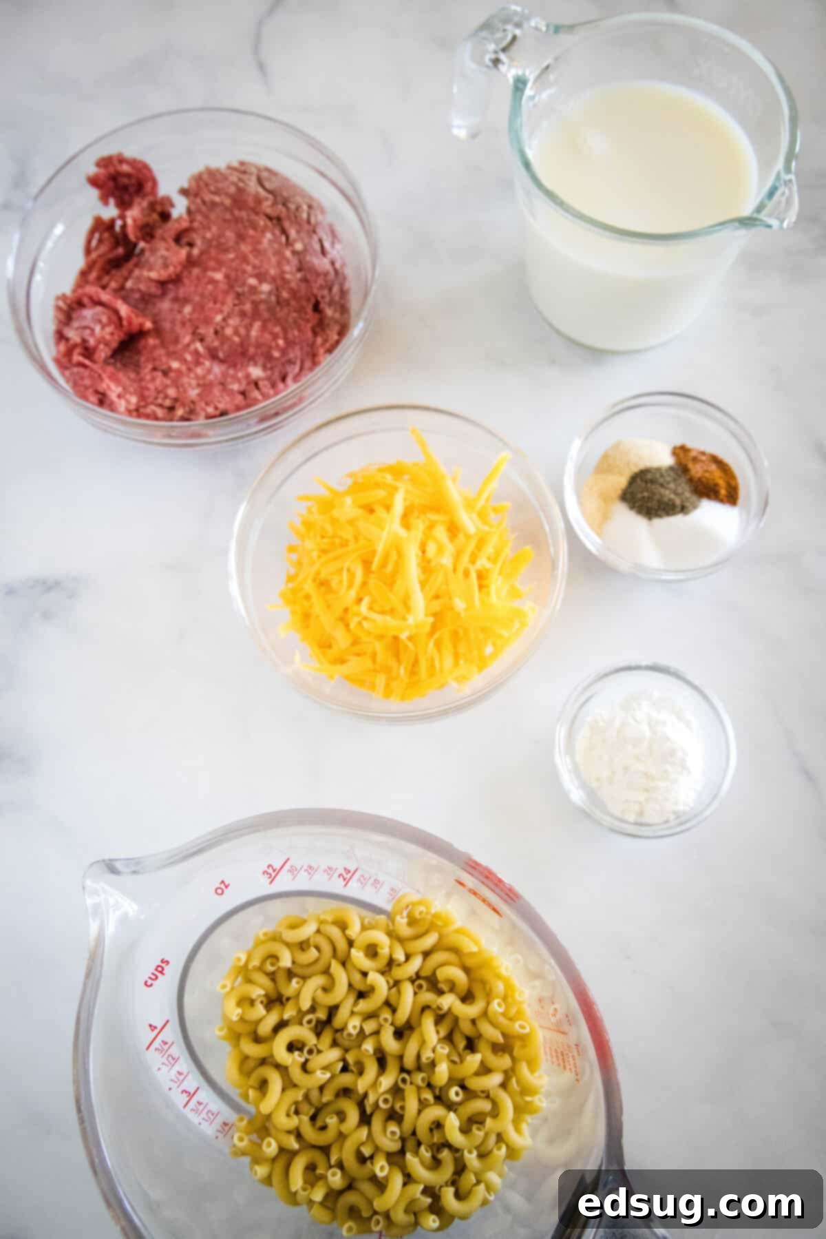 Homestyle Cheeseburger Macaroni 3 Array of ingredients for homemade cheeseburger macaroni including ground beef, elbow macaroni, shredded cheese, milk, water, and various spices