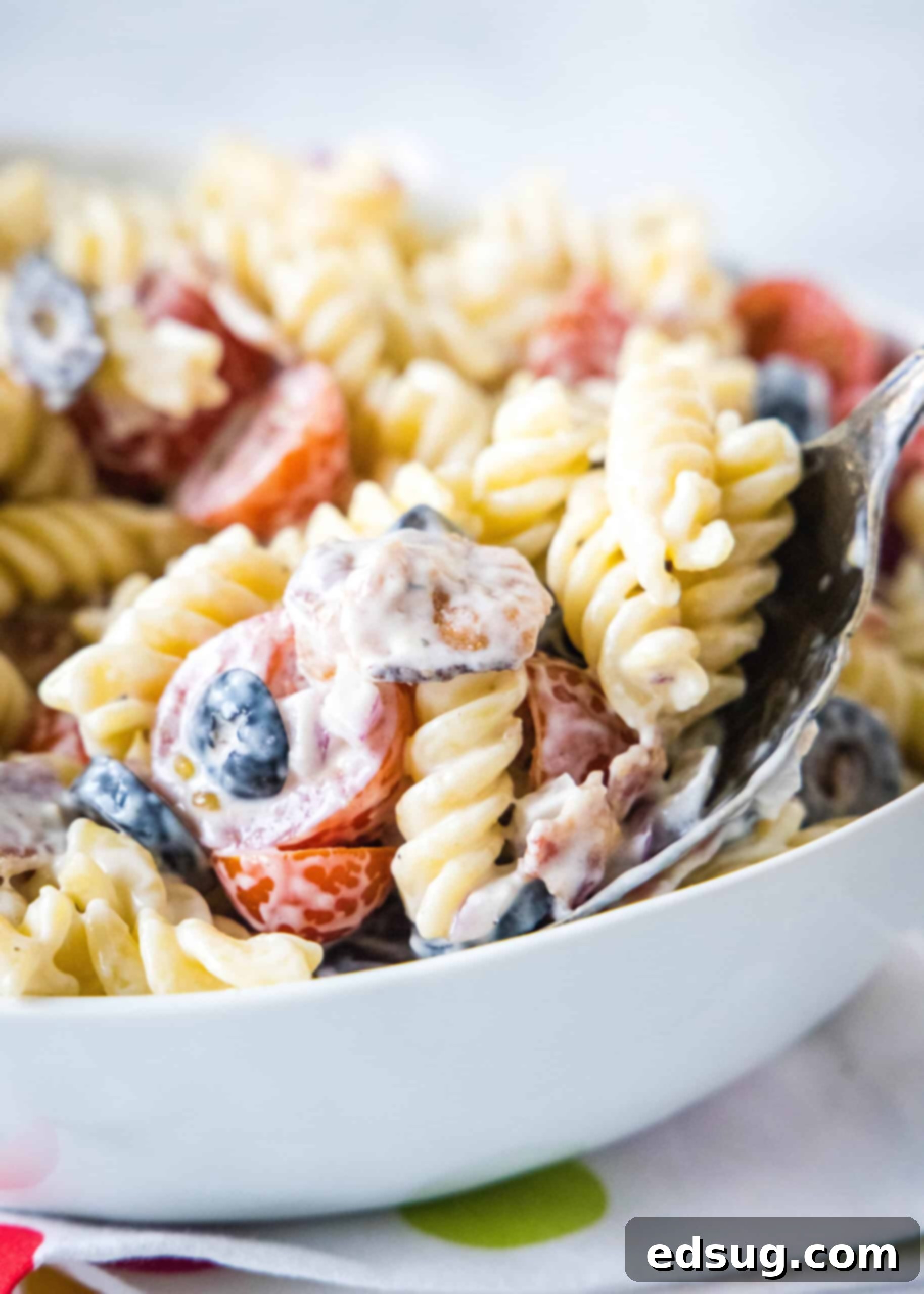A large serving spoon scooping a portion of creamy ranch pasta salad from a white bowl, ready to be served.