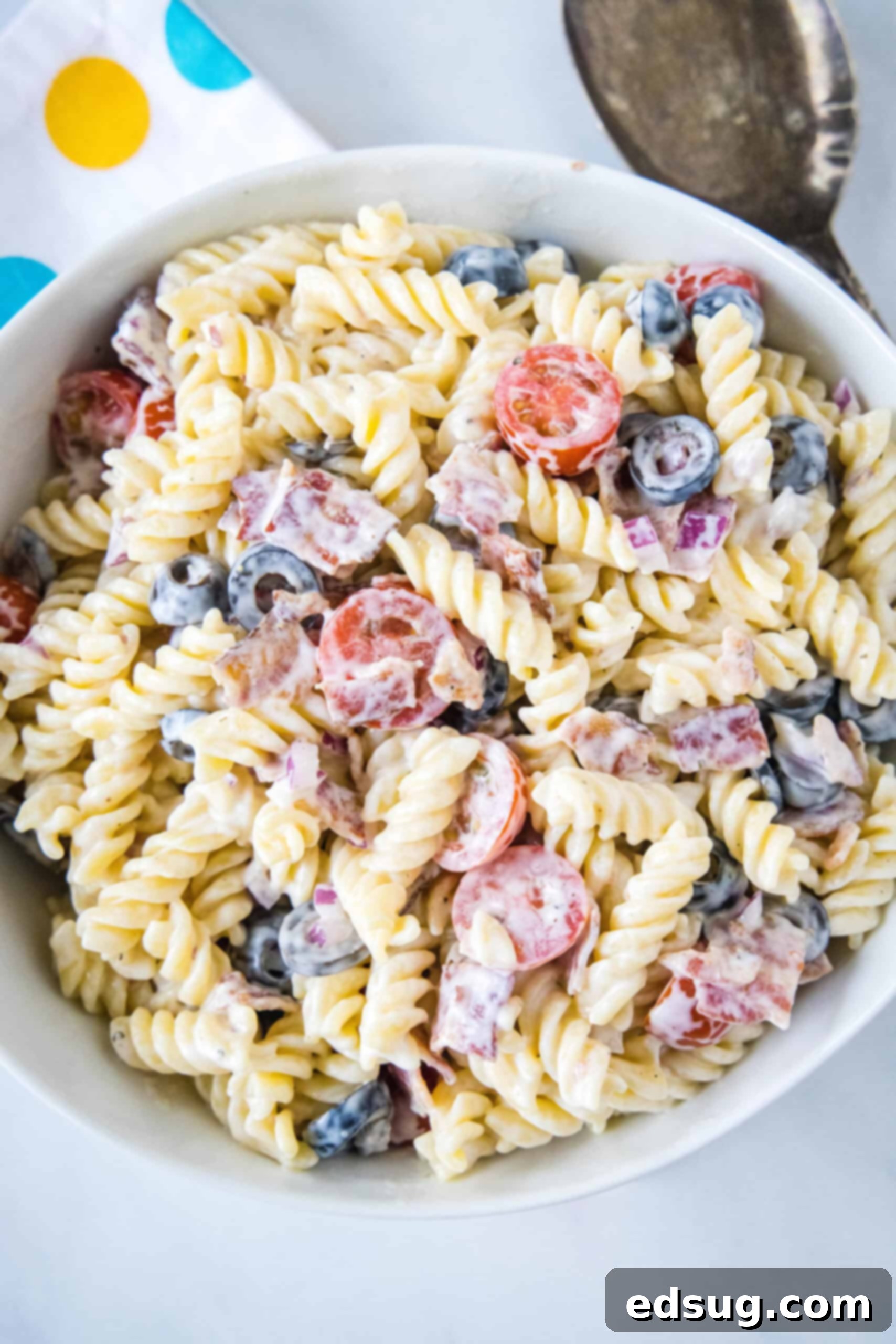 Overhead view of a white bowl filled with creamy ranch pasta salad, garnished with fresh herbs and crumbled bacon.