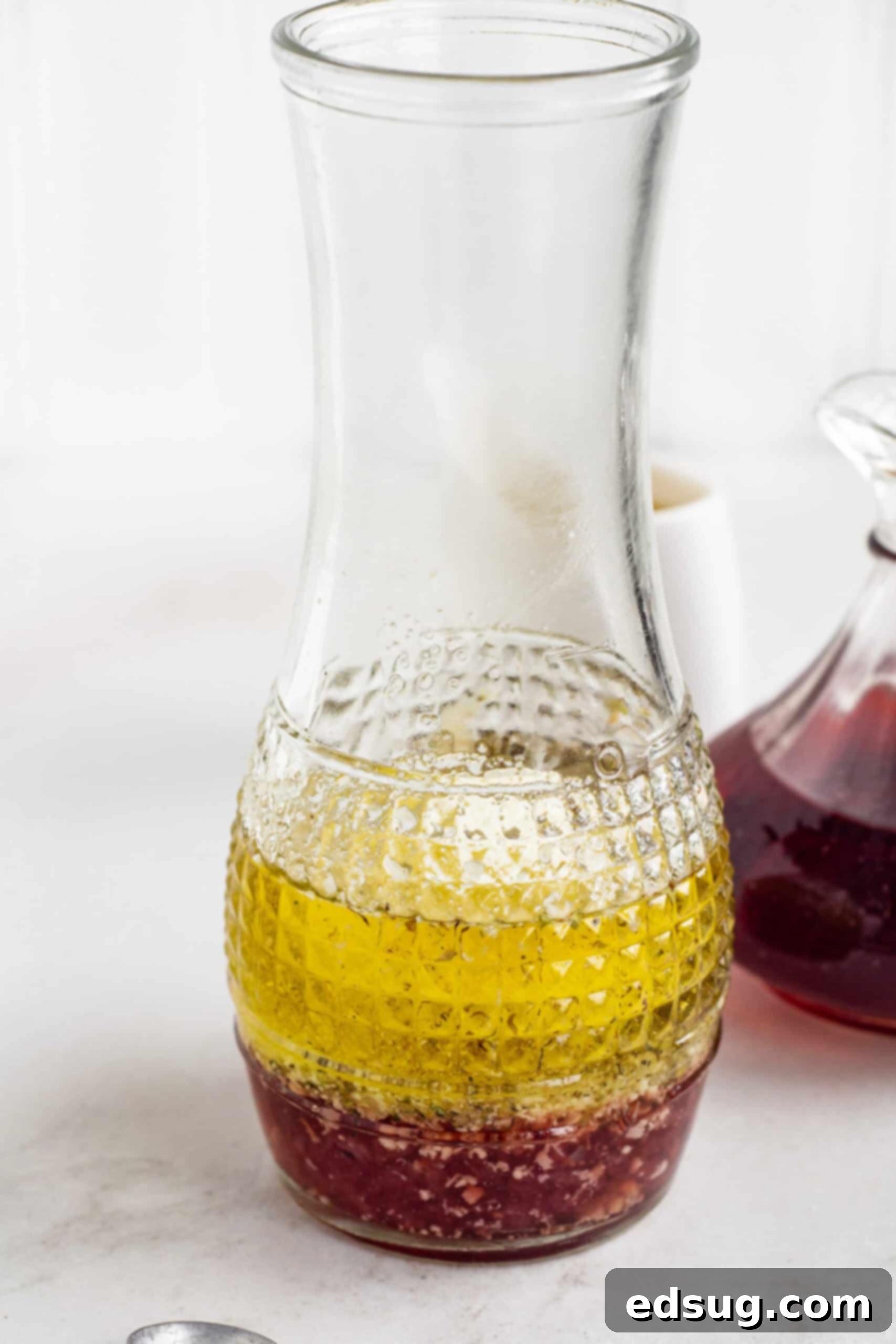 Red wine vinaigrette ingredients inside a glass carafe, showing fresh herbs and spices ready for mixing.