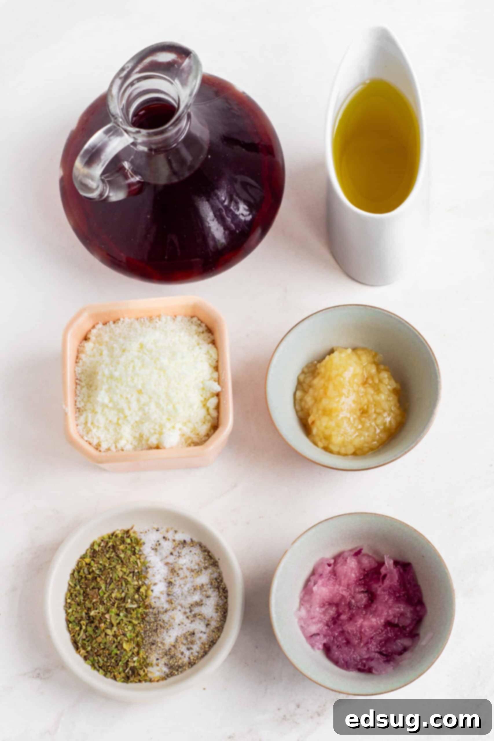 Close-up of fresh ingredients for red wine vinaigrette, including olive oil, red wine vinegar, grated Parmesan, and chopped herbs.