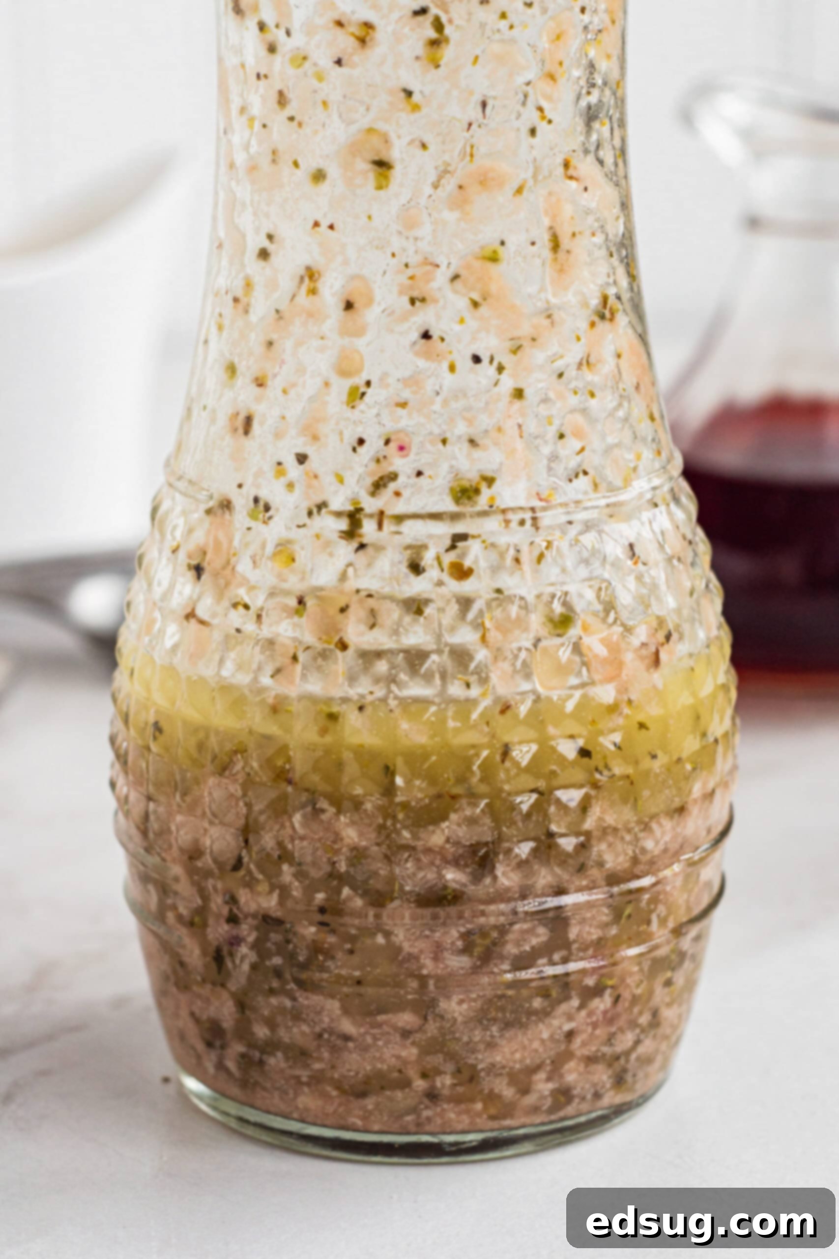 A glass carafe of perfectly emulsified red wine vinaigrette, showcasing its smooth texture and rich color, ready for use.