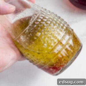 A hand holding up a carafe of red wine vinaigrette, showcasing its beautiful color and smooth texture.