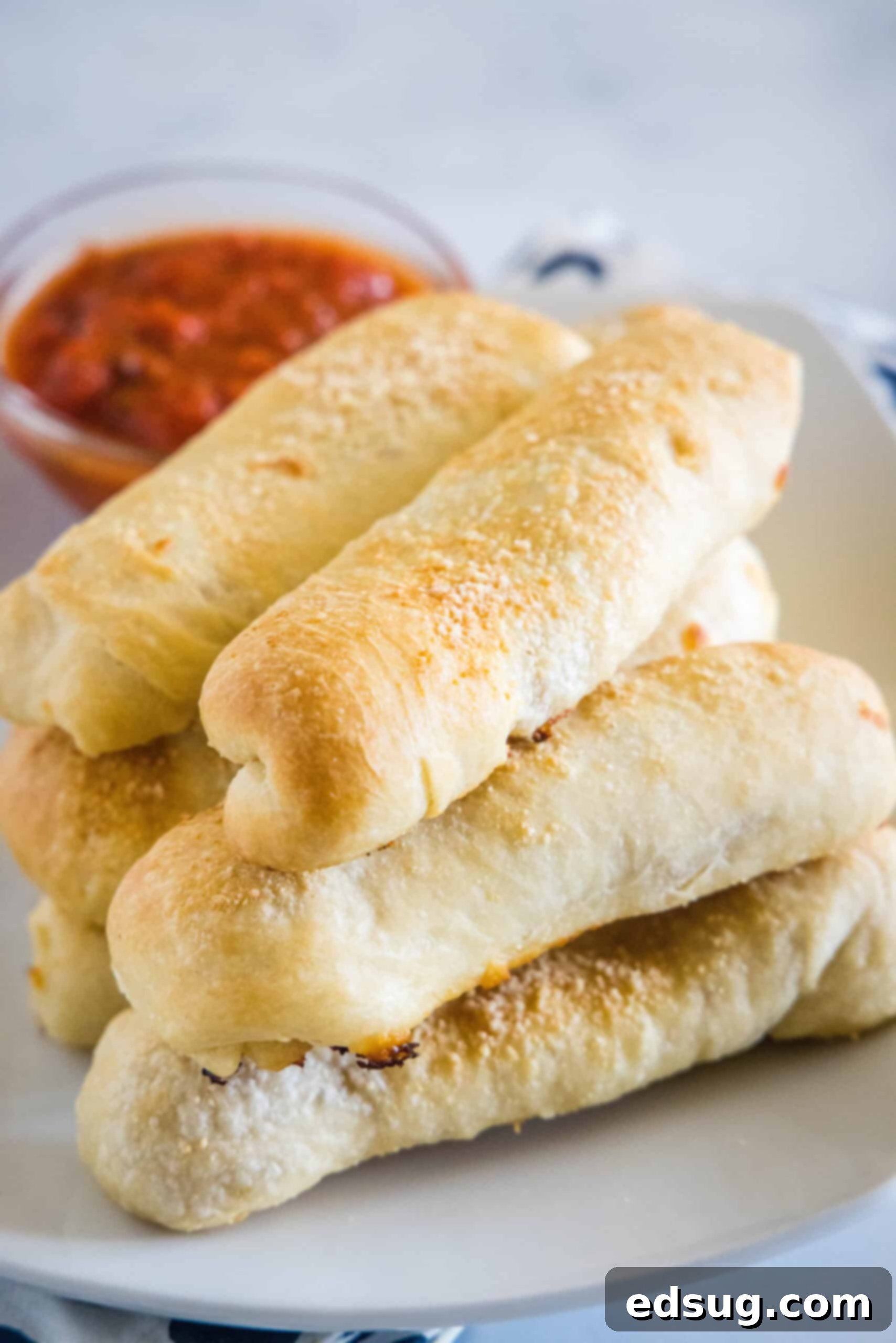 These pepperoni rolls are an easy snack made from soft, fluffy pizza dough filled with melty mozzarella cheese and juicy pepperoni slices. Pepperoni rolls stacked on a plate with a small bowl of marinara sauce in the background.