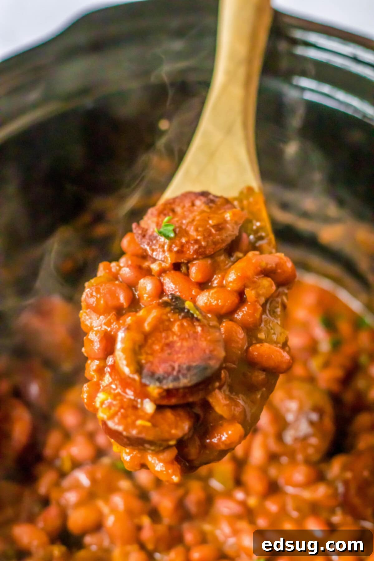 Red beans and sausage cooking in a crockpot, with a wooden spoon removing a spoonful.