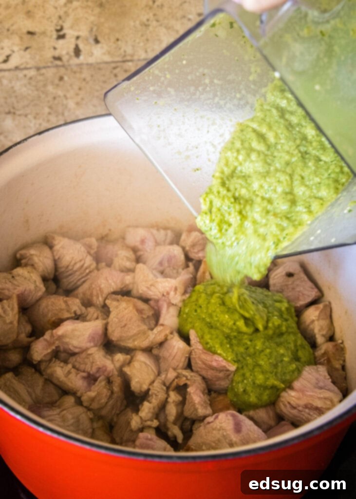 Pork Verde 4 Pouring homemade green chili sauce into a pot with browned pork shoulder.