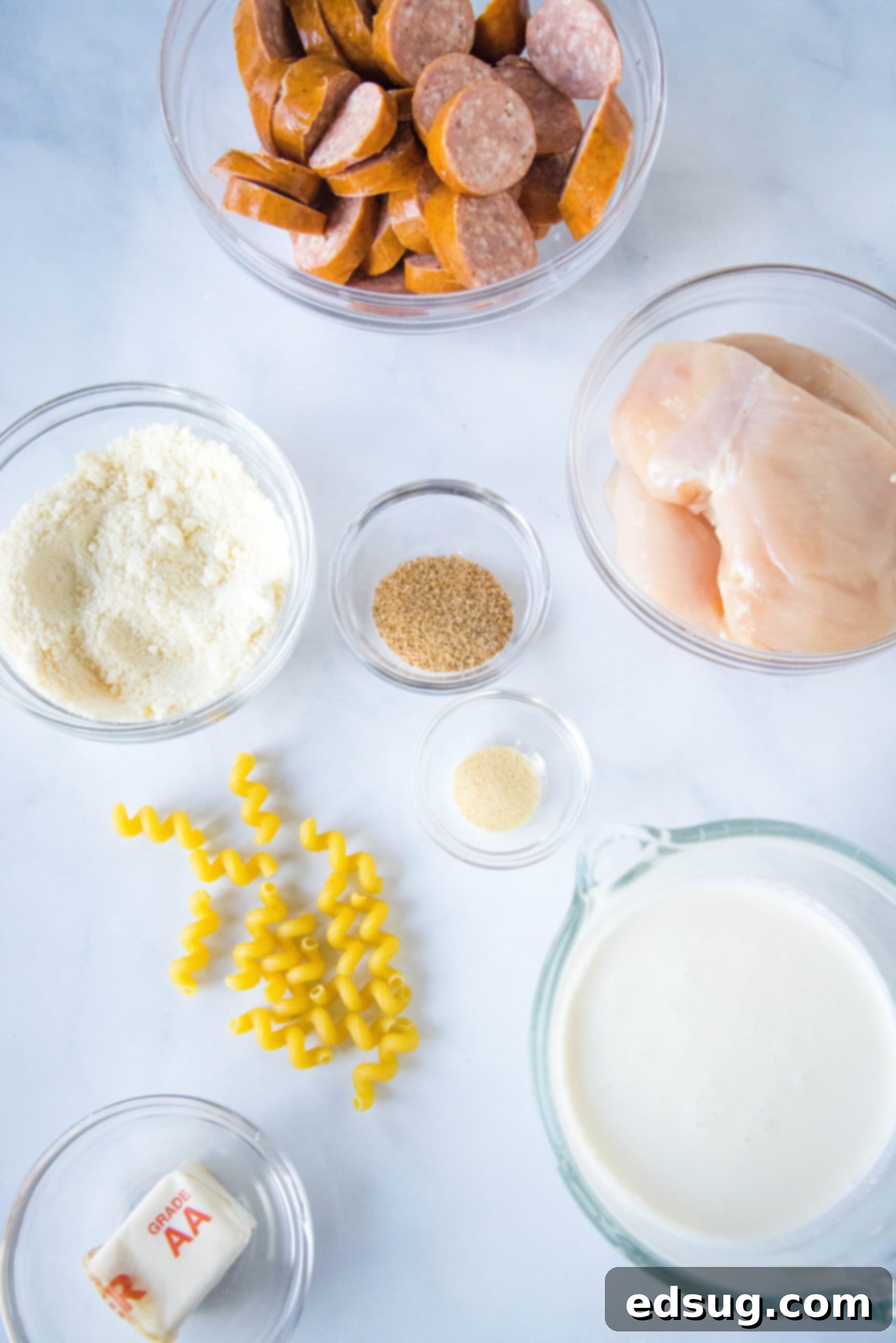 This creamy crockpot Cajun chicken pasta is easy to make in the slow cooker with spicy sausage and a rich, cheesy sauce. Just add pasta! A flat lay photograph of all the raw ingredients for Cajun chicken pasta laid out on a dark surface: chicken, sausage, cream, cheese, spices, and butter.