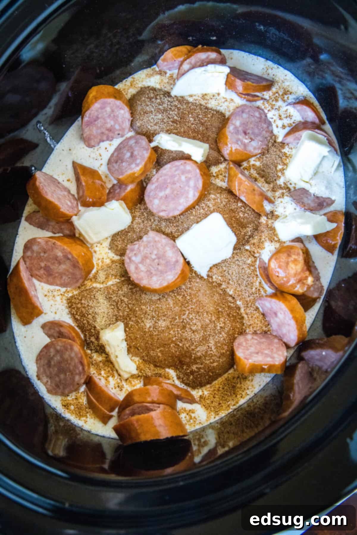 This creamy crockpot Cajun chicken pasta is easy to make in the slow cooker with spicy sausage and a rich, cheesy sauce. Just add pasta! Chicken, sausage, and spices arranged in a slow cooker with heavy cream and Parmesan at the bottom.