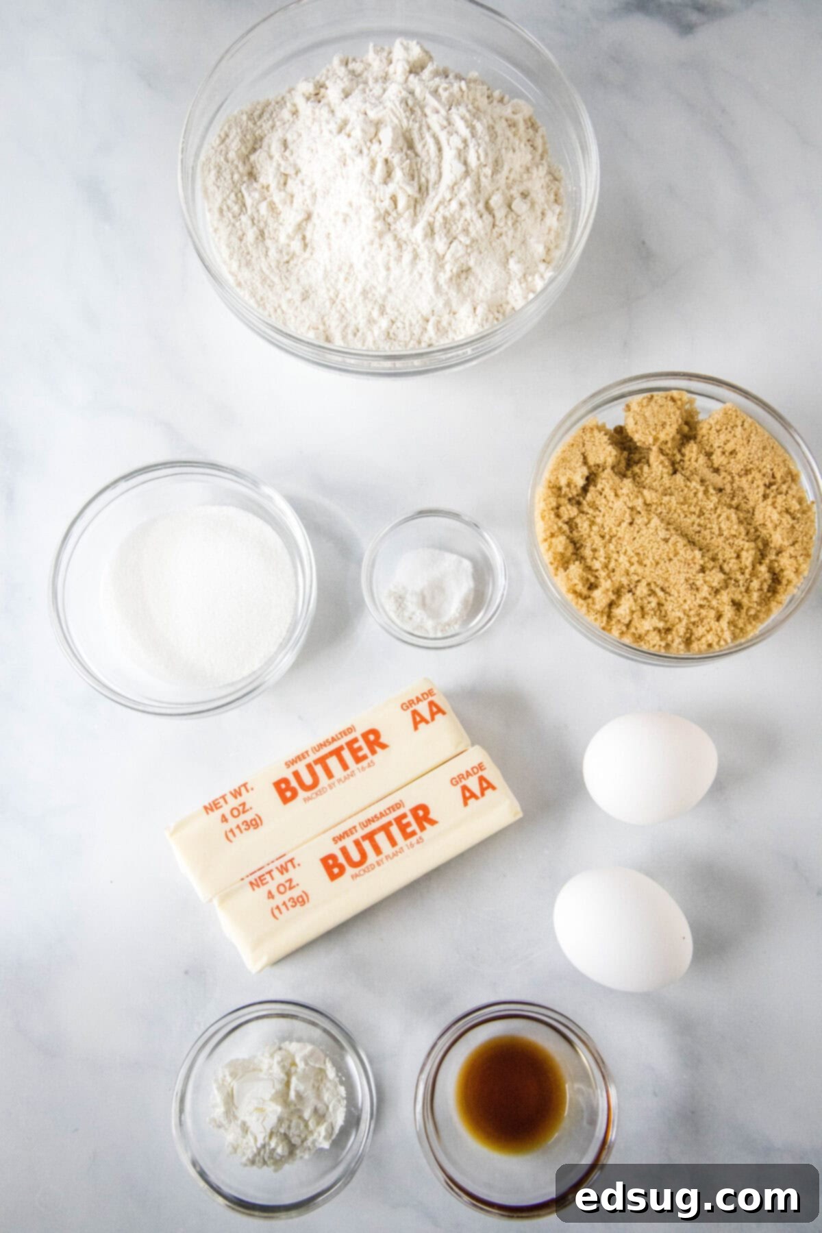 These cookie dough cookies are bakery-style sugar cookies topped with creamy cookie dough frosting, edible cookie dough, and chocolate chips! A collection of ingredients for the cookie base, including flour, sugars, butter, and eggs, neatly arranged on a counter.