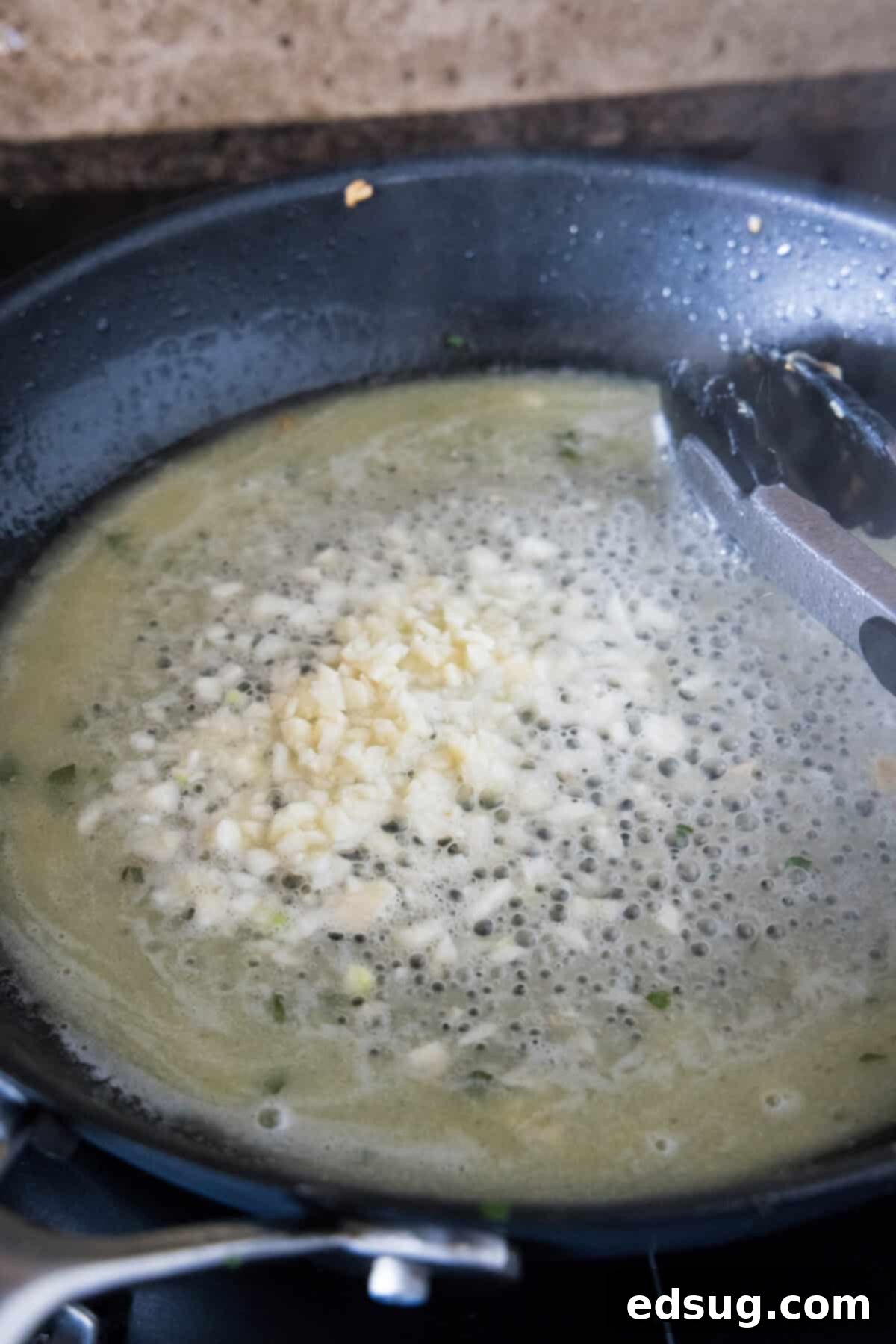 White wine being poured into the skillet to deglaze and start the scampi sauce.