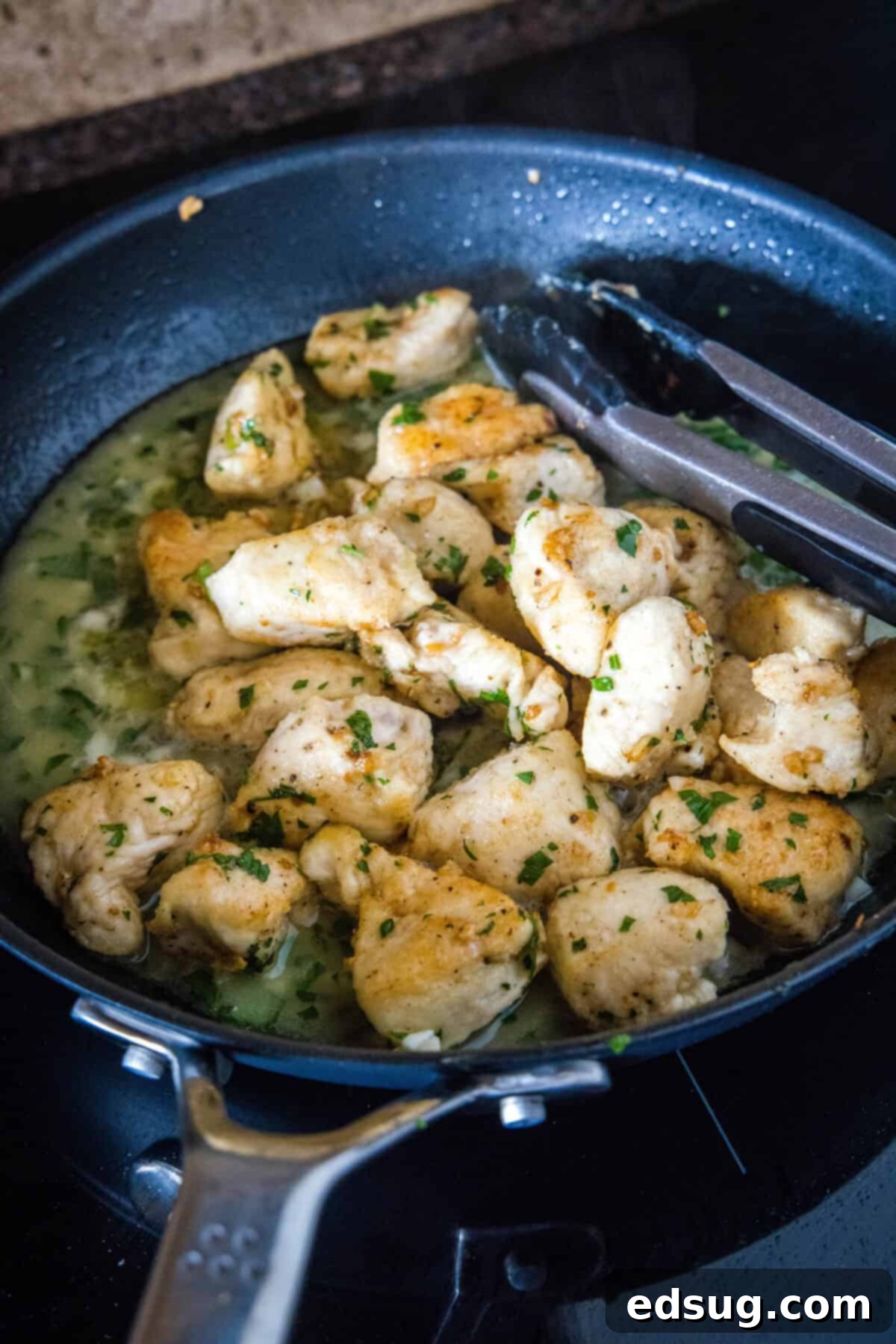 Seared chicken pieces being returned to the scampi sauce in the skillet.