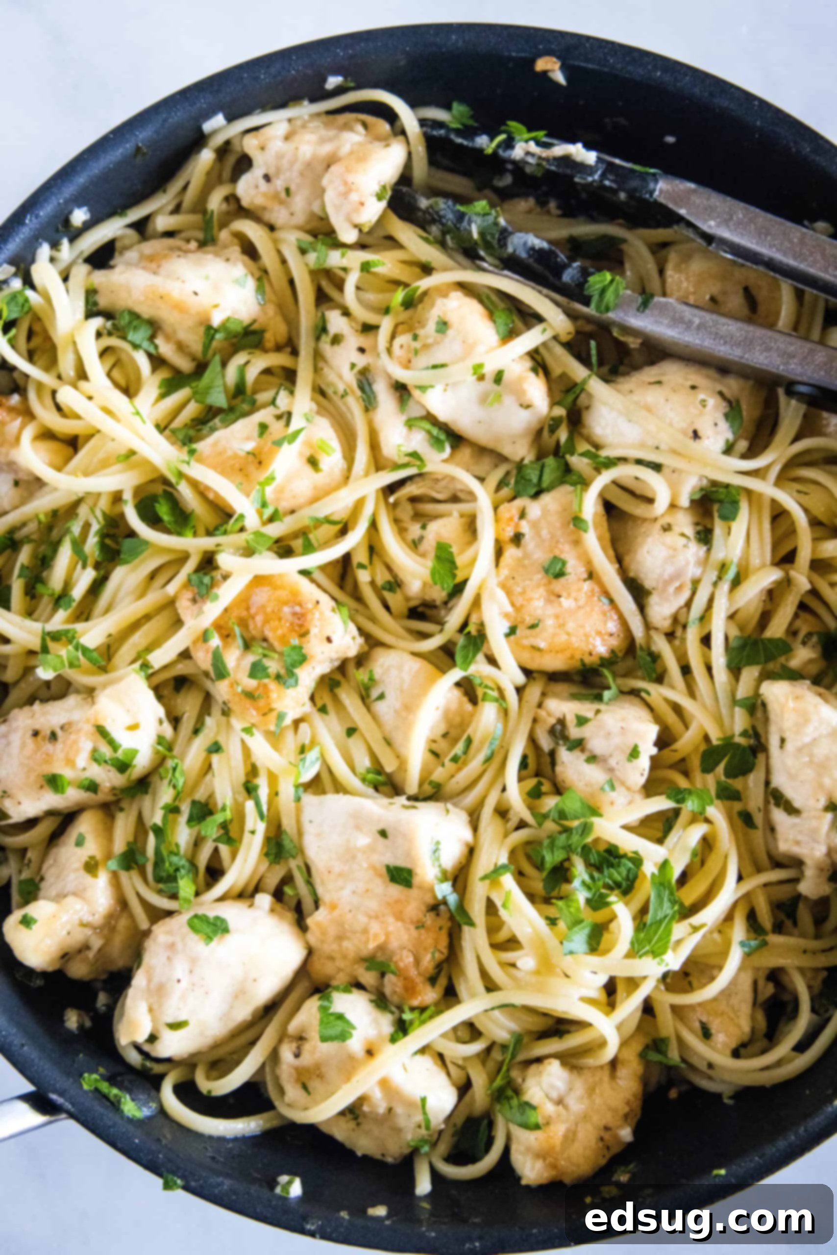 Overhead view of chicken scampi with spaghetti being tossed in a skillet.
